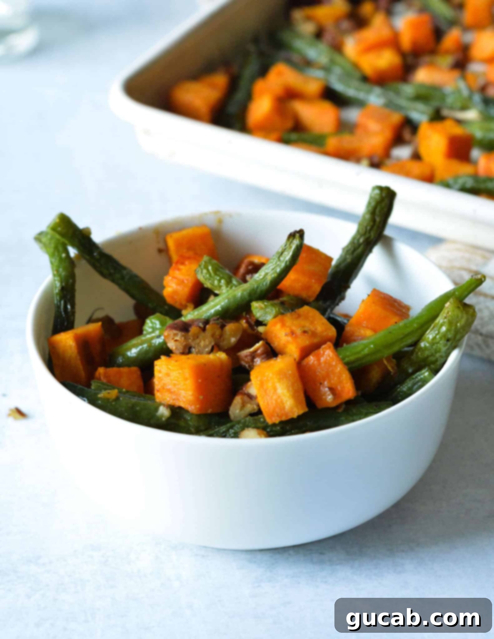 Perfectly Roasted Green Beans and Sweet Potatoes 10 A serving bowl filled with a generous portion of roasted green beans, sweet potatoes, and pecans, ready to be enjoyed.