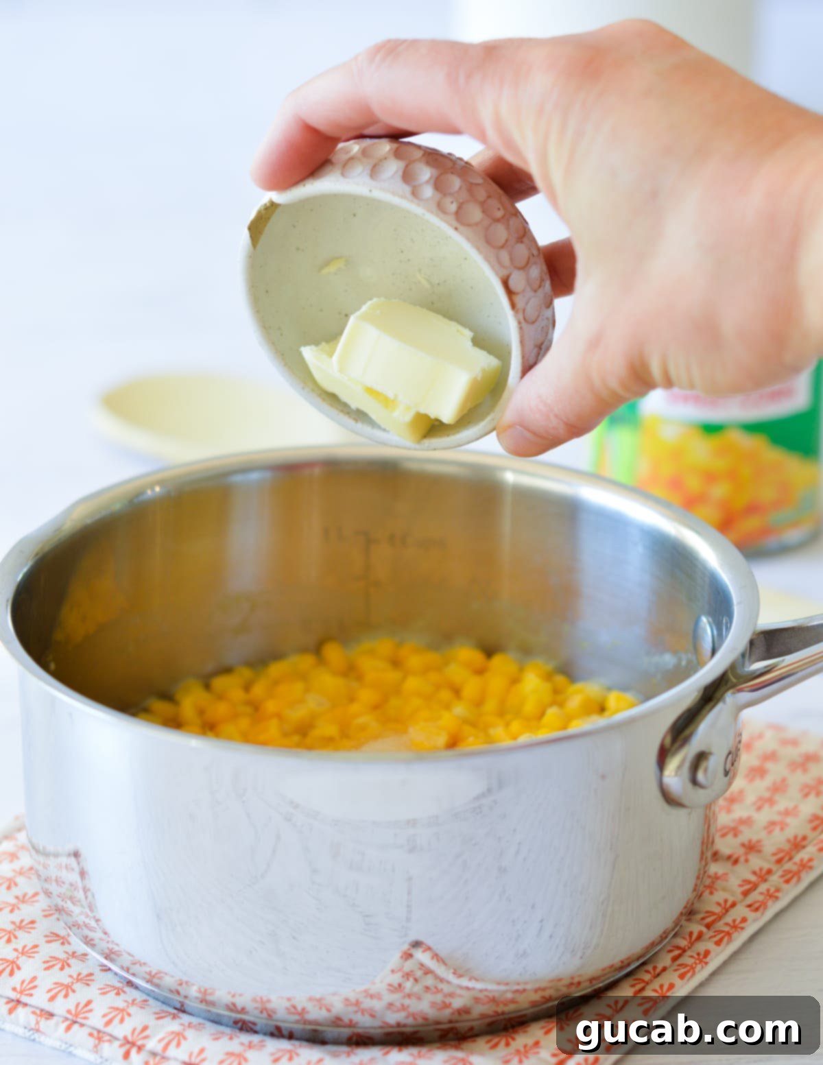 A hand adding a knob of unsalted butter to the corn in the saucepan.