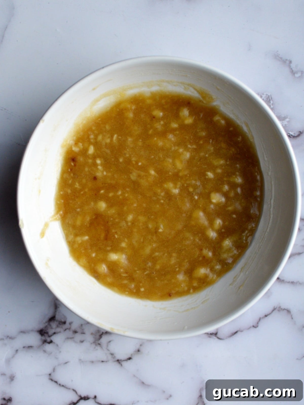 a bowl of mashed banana, sugar, and oil being mixed