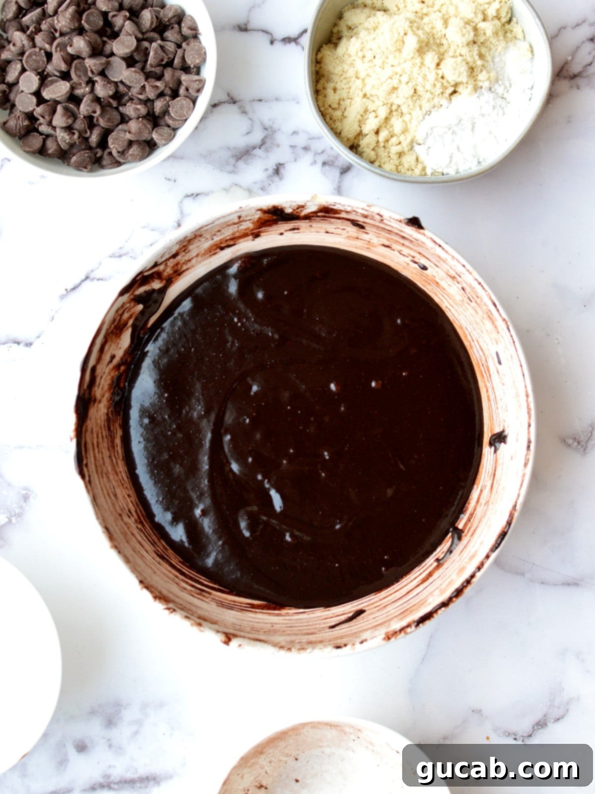 A bowl of glossy, rich gluten-free brownie batter, showing the smooth consistency after eggs are incorporated.