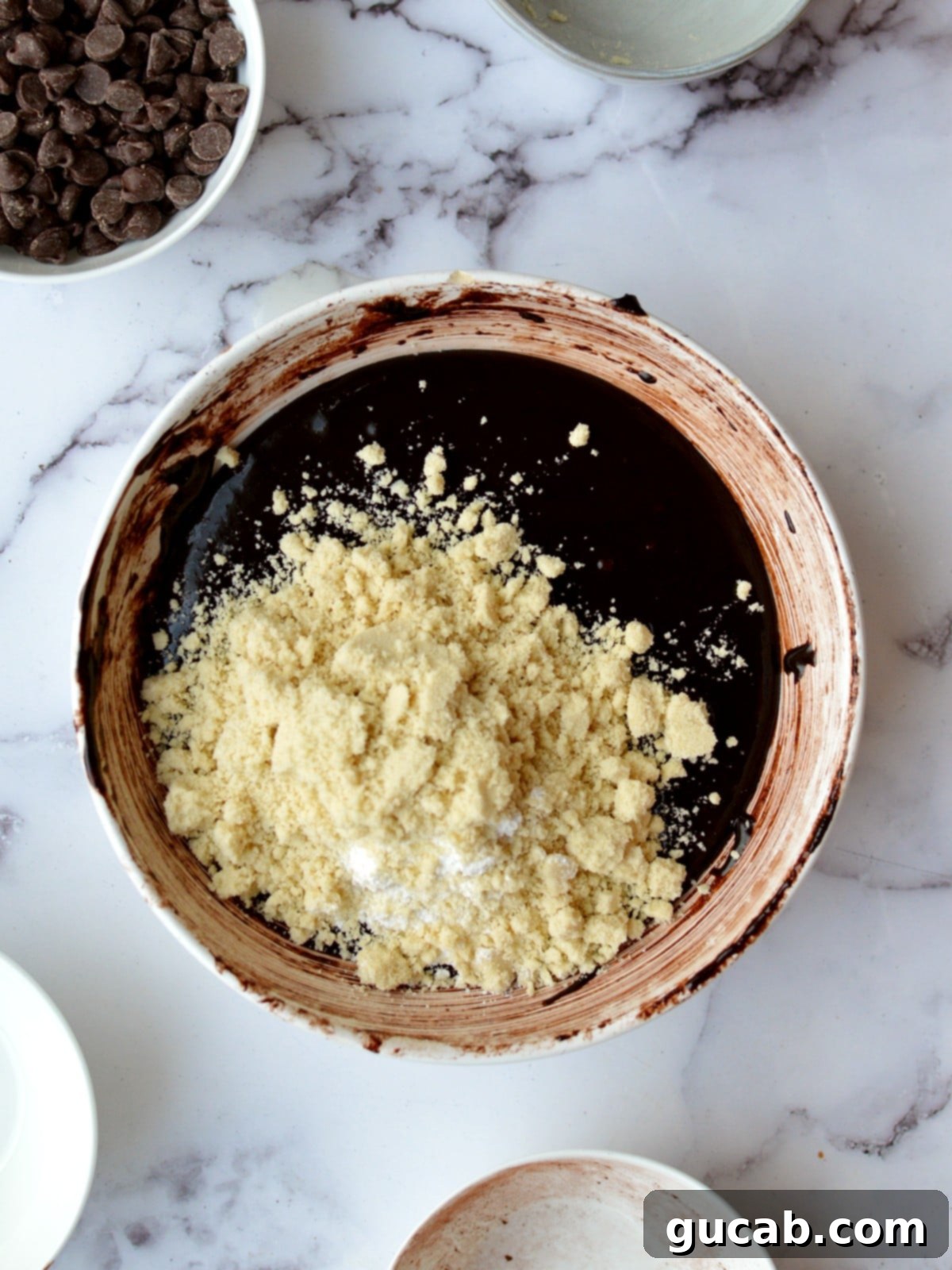 Brownie batter in a bowl with almond flour sprinkled on top, ready to be mixed.
