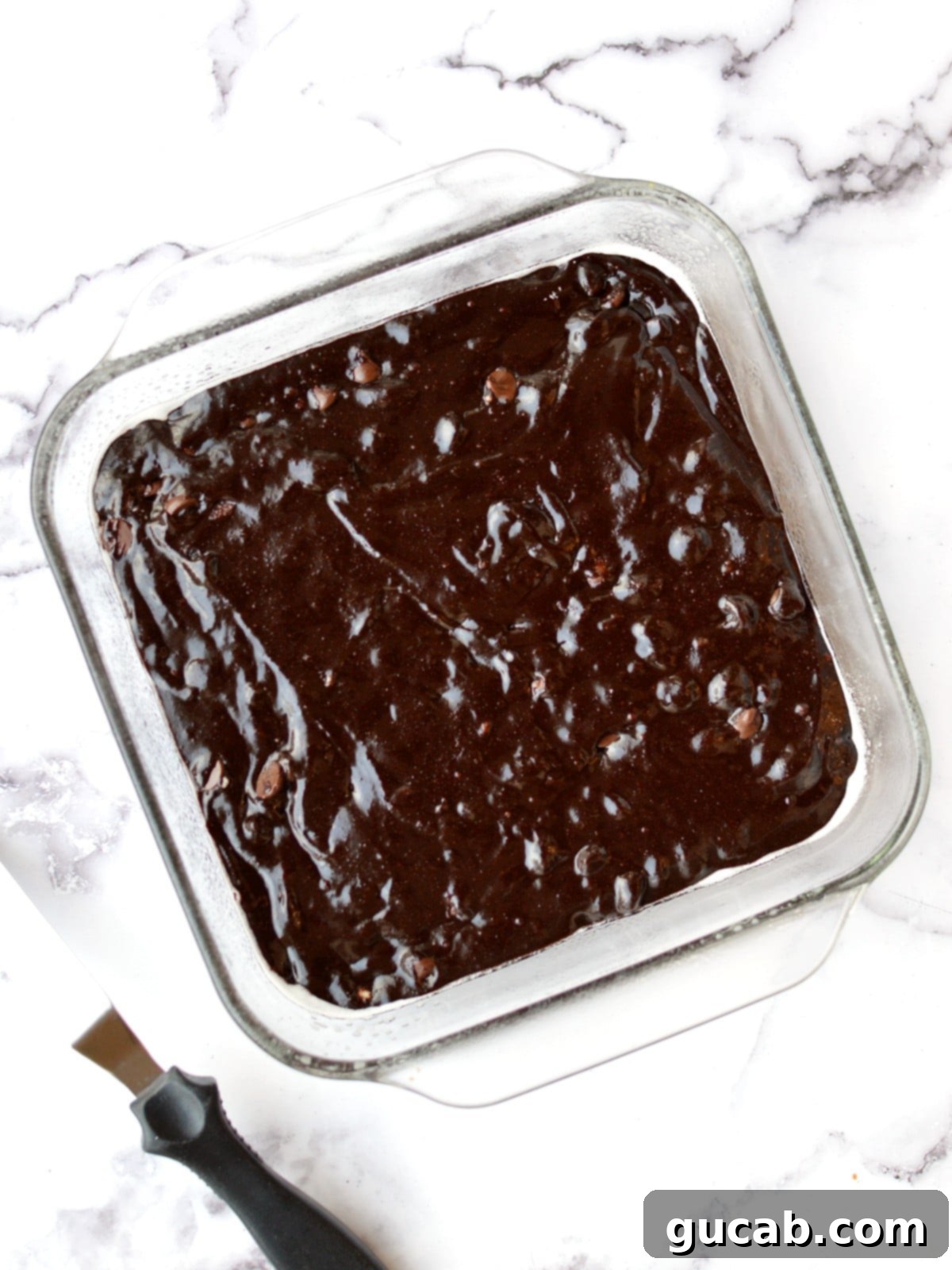 Unbaked brownie batter spread evenly in a square baking dish, ready for the oven.