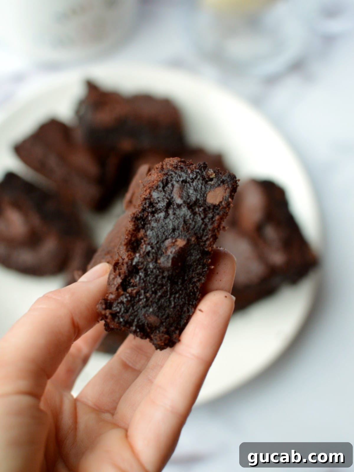 A hand holding a single, perfectly cut almond flour brownie, showing its thick, fudgy center.