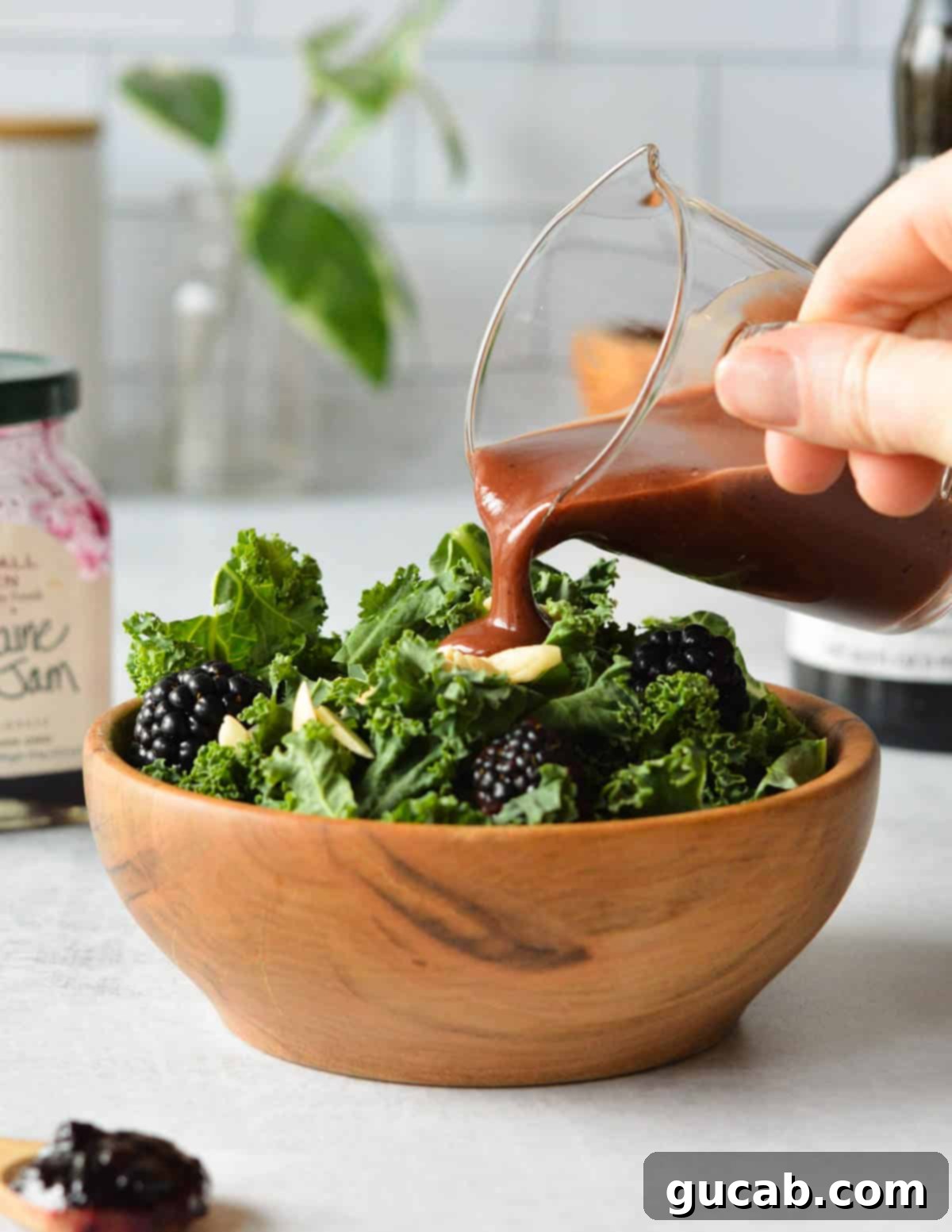 pouring balsamic dressing onto a kale salad with blackberries and almonds.