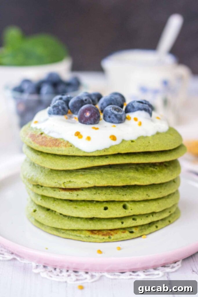 A stack of fluffy matcha pancakes, drizzled with maple syrup and garnished with fresh berries.