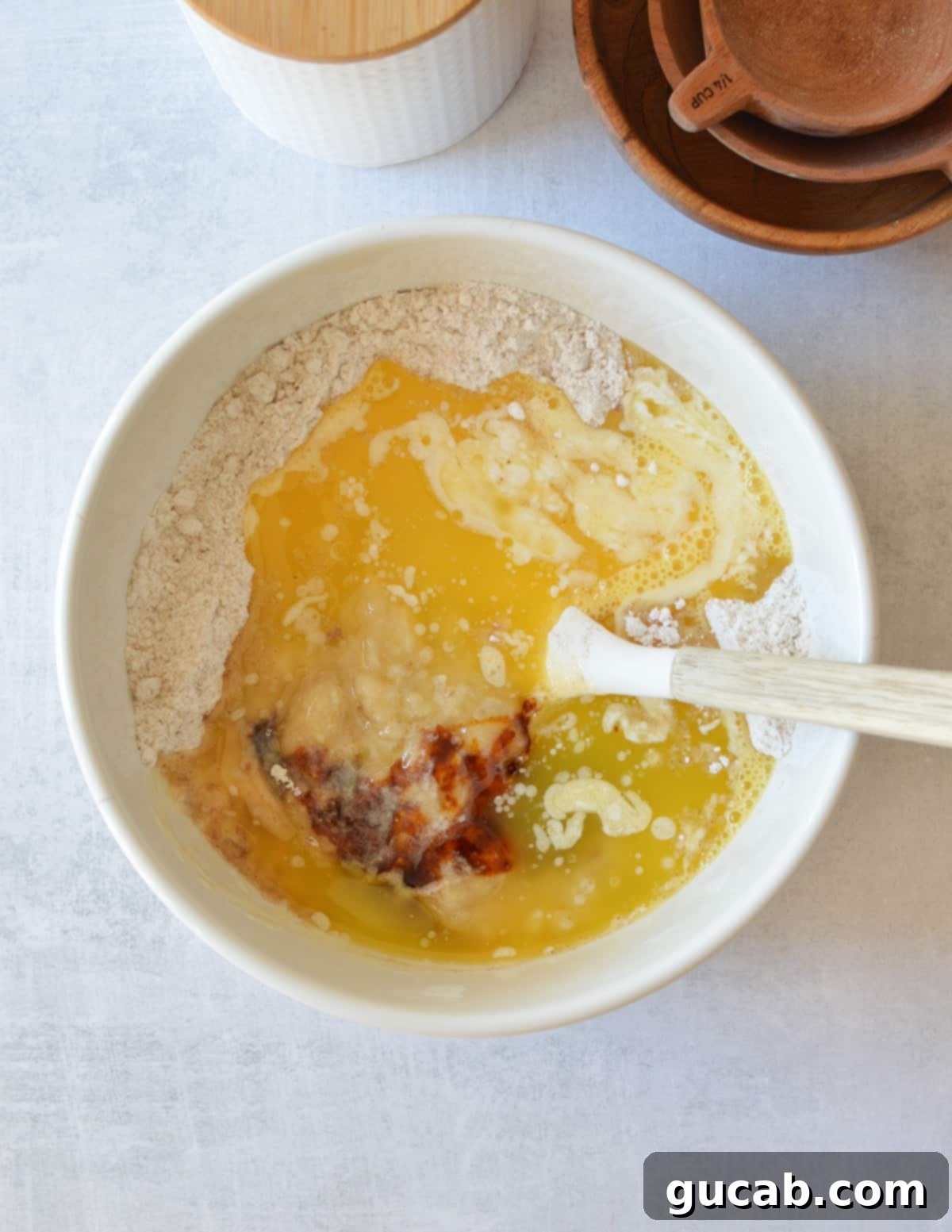 a bowl of gluten-free flour, sugar, melted butter, eggs, and mashed banana.