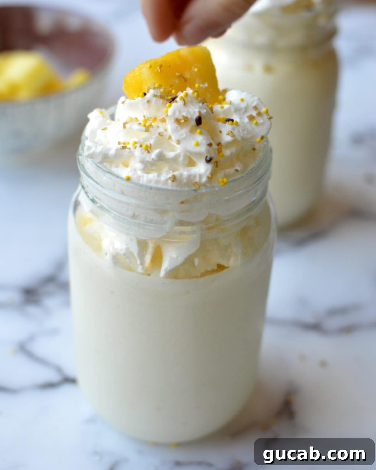 A creamy pineapple milkshake served in a tall glass, topped with a generous swirl of whipped cream and a fresh pineapple wedge garnish.