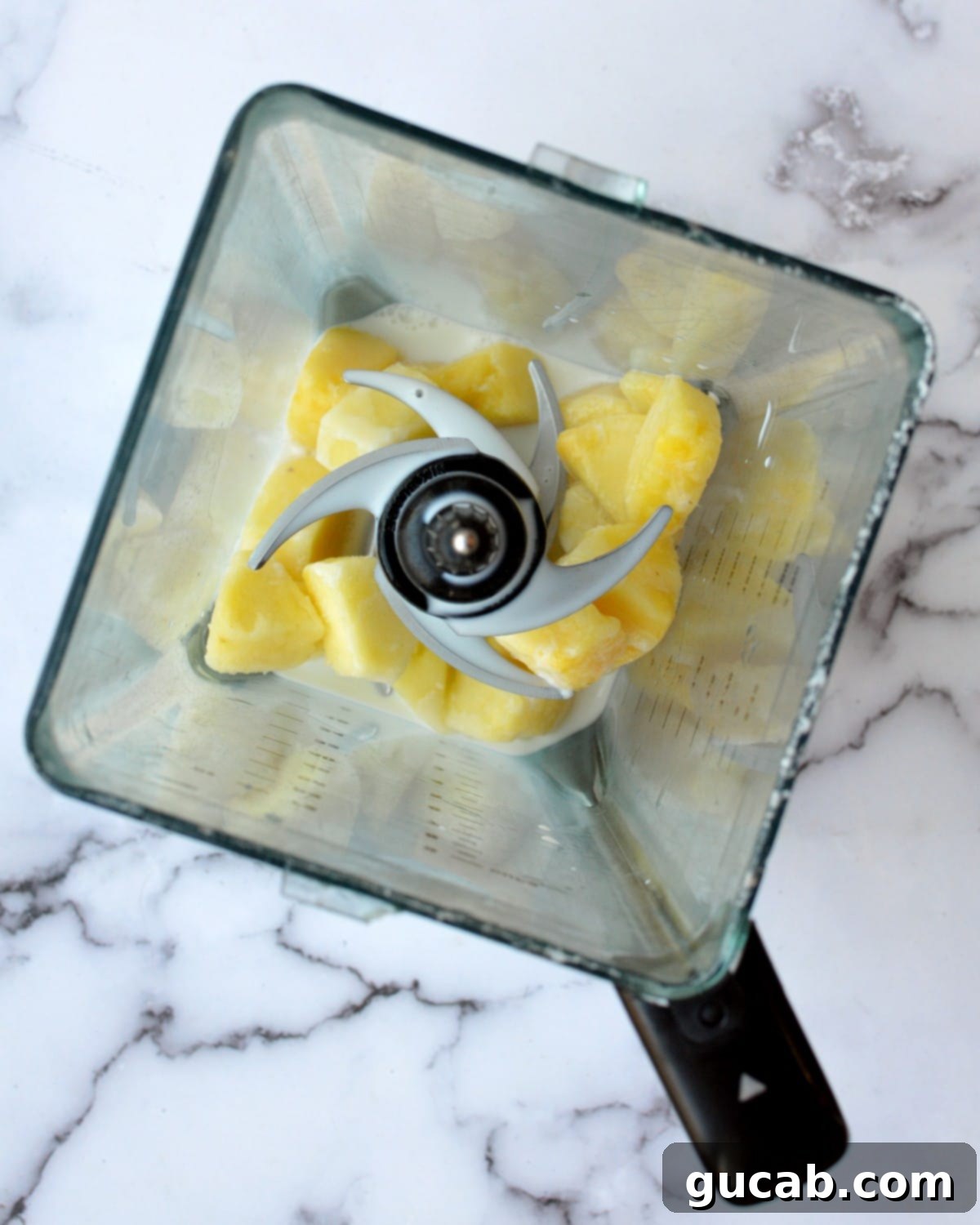 A high-speed blender filled with frozen pineapple, whole milk, and pineapple juice, ready to be blended for a creamy milkshake.