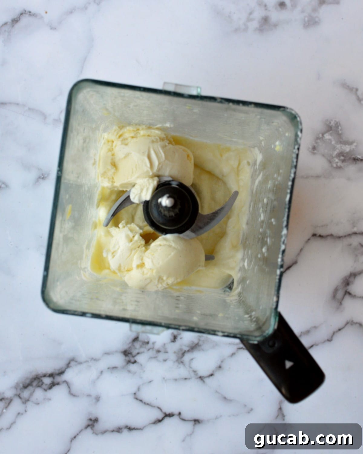 A blender containing the blended pineapple and milk mixture, with a scoop of vanilla ice cream just added on top.