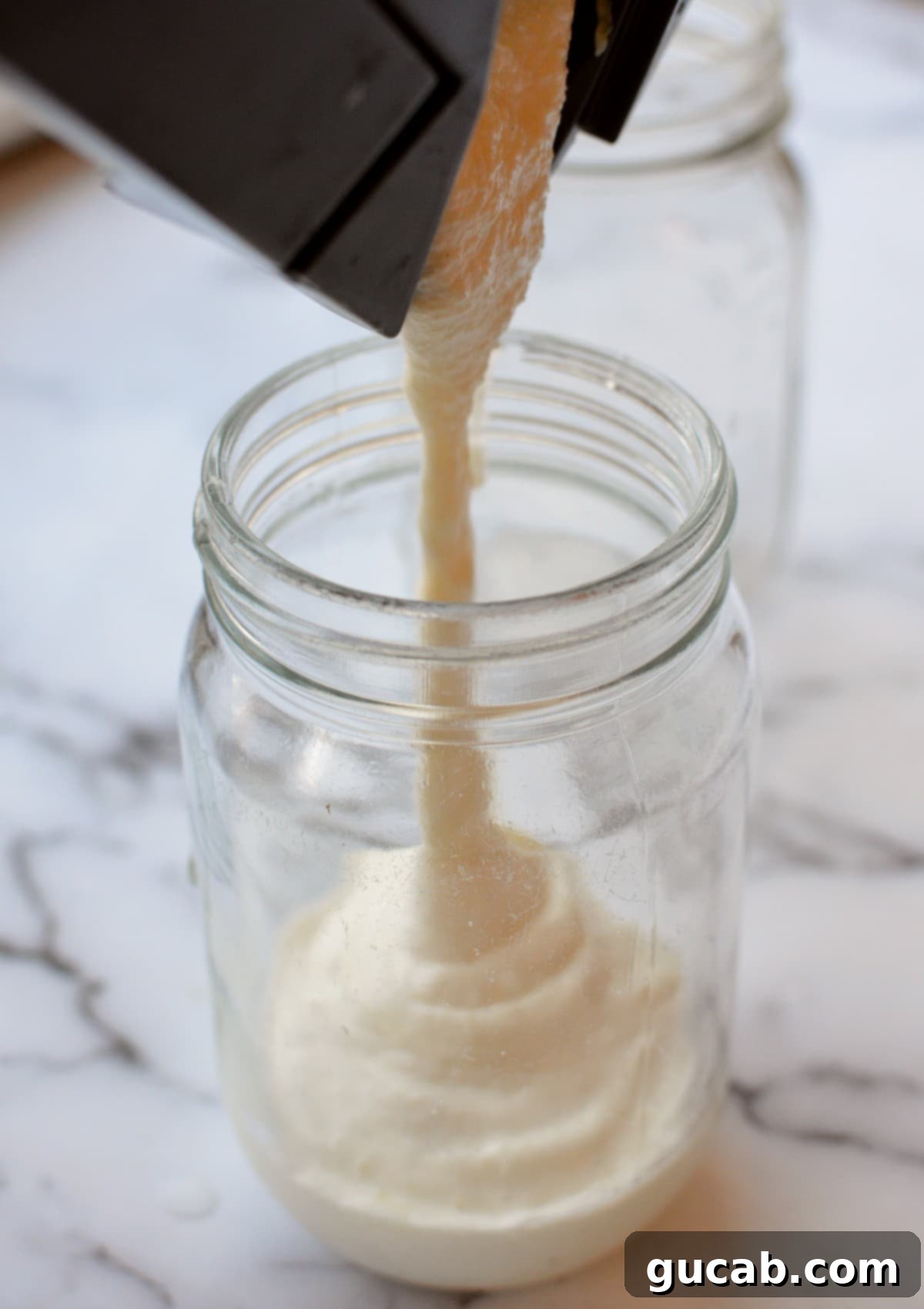 A thick, creamy pineapple milkshake being poured from a blender into a tall glass.
