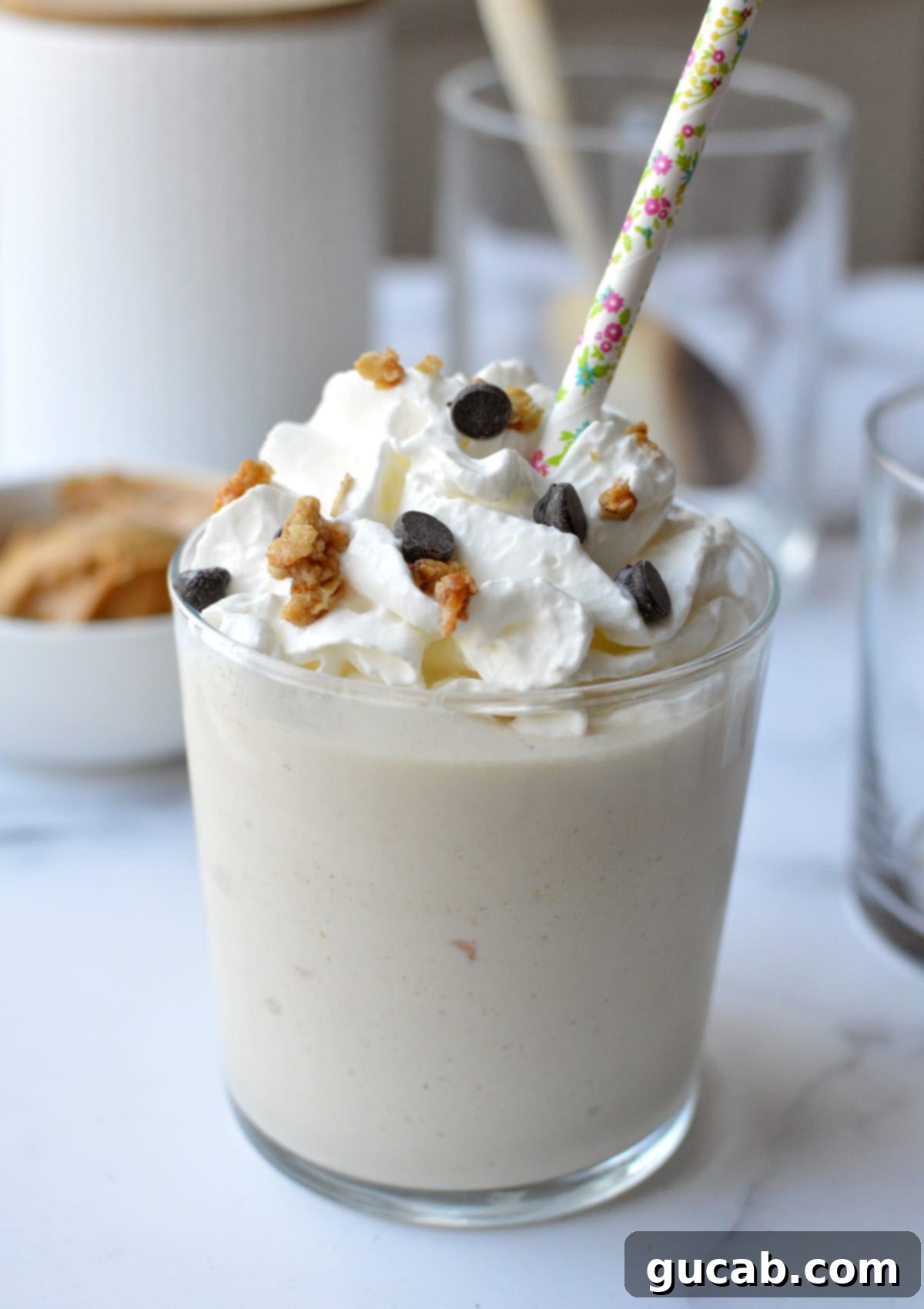 A tall glass of peanut butter milkshake crowned with whipped cream and a sprinkle of chopped peanuts.