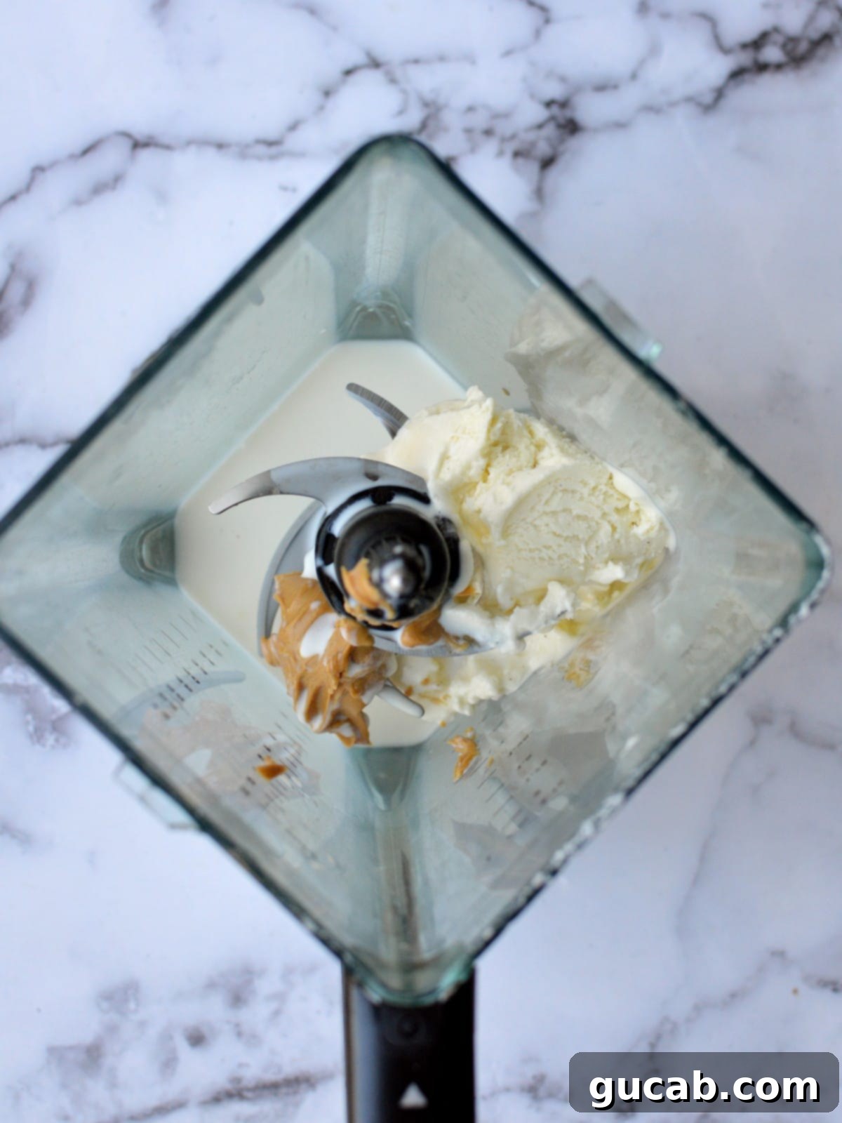 A blender filled with spoonfuls of creamy peanut butter, scoops of vanilla ice cream, and a splash of milk, ready for blending.