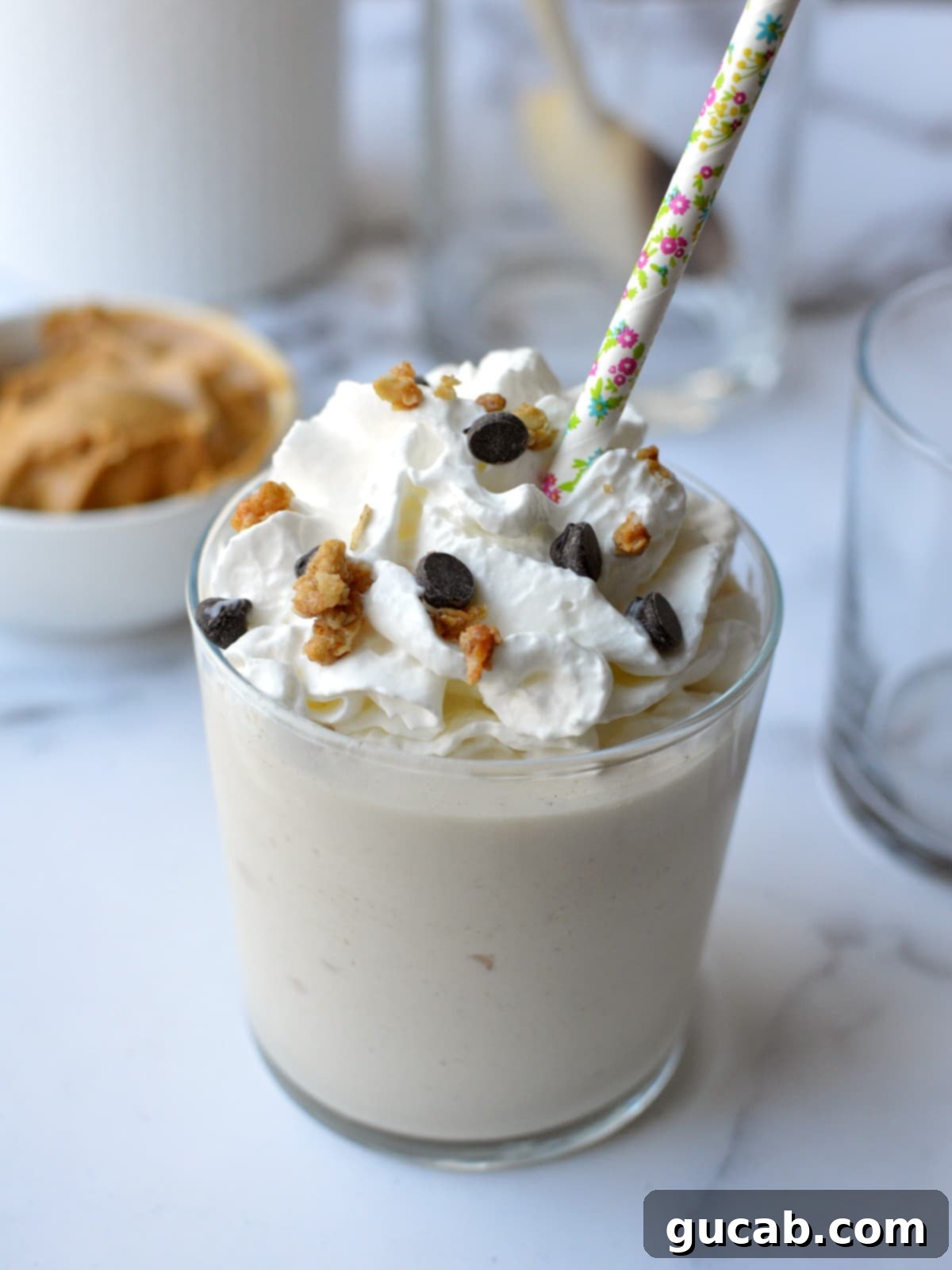 A beautifully presented peanut butter shake with a generous topping of whipped cream and a sprinkle of chocolate shavings.