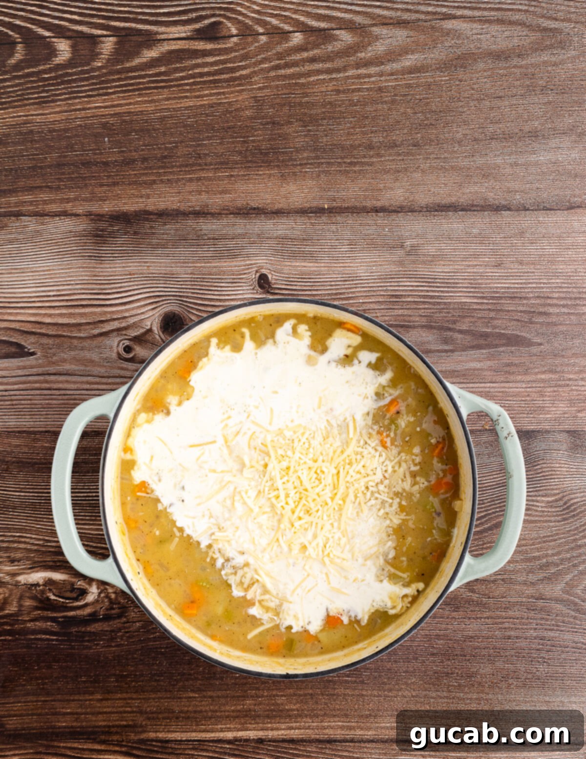 chicken broth, cream, veggies, and potatoes cooking in a dutch oven.