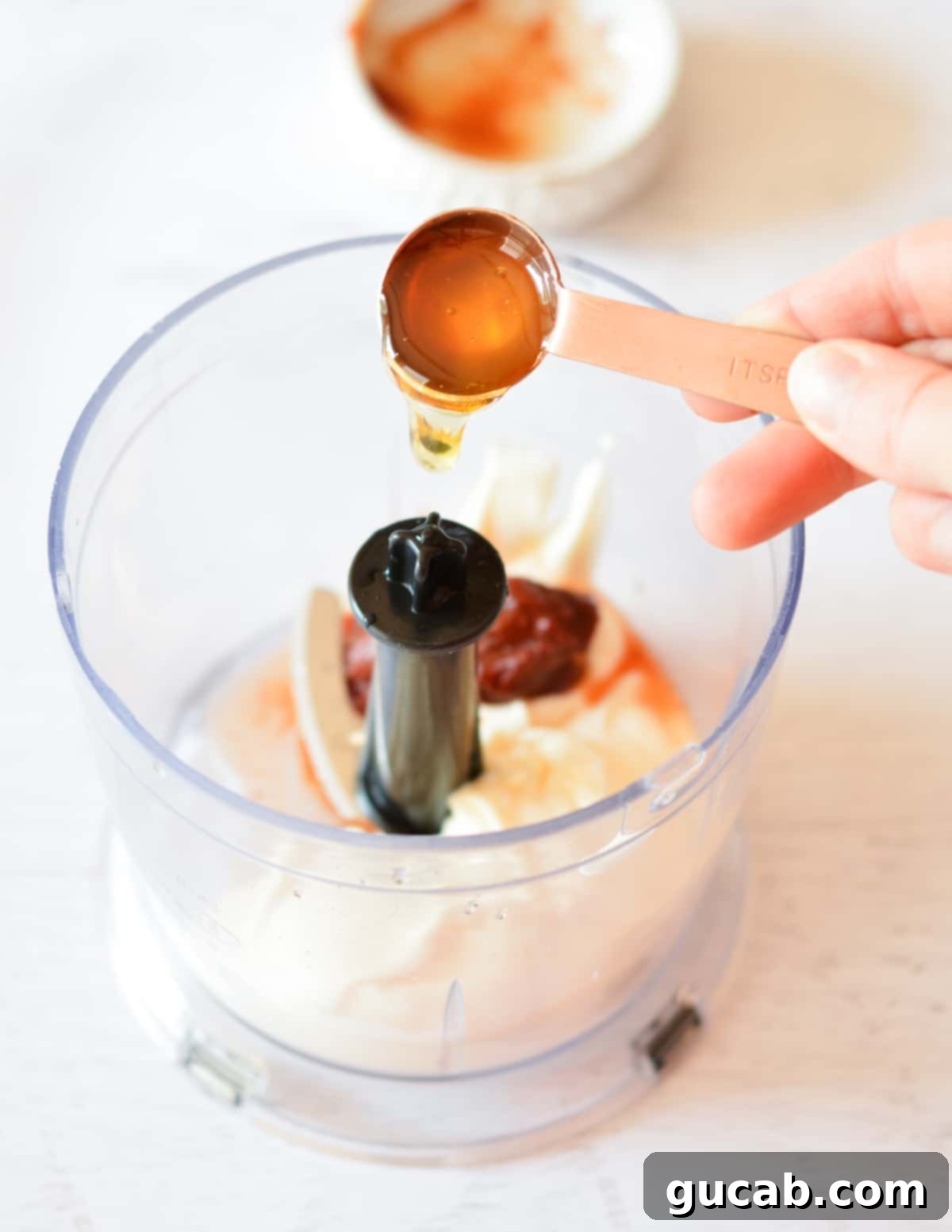 Homemade Chipotle Mayo 7 pouring honey into a food processor with mayo and chipotles.