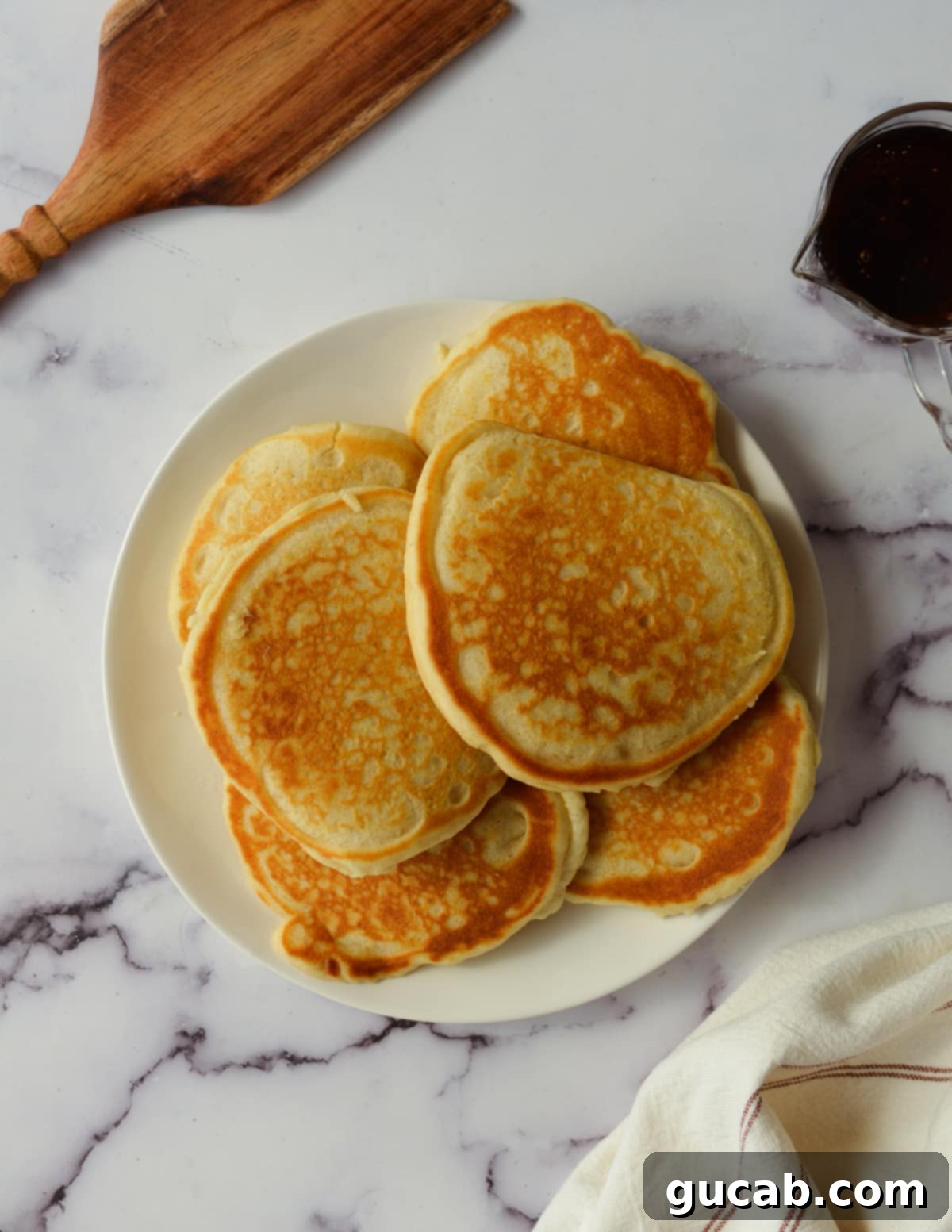 Three golden gluten-free pancakes artfully arranged on a white plate, ready for toppings.