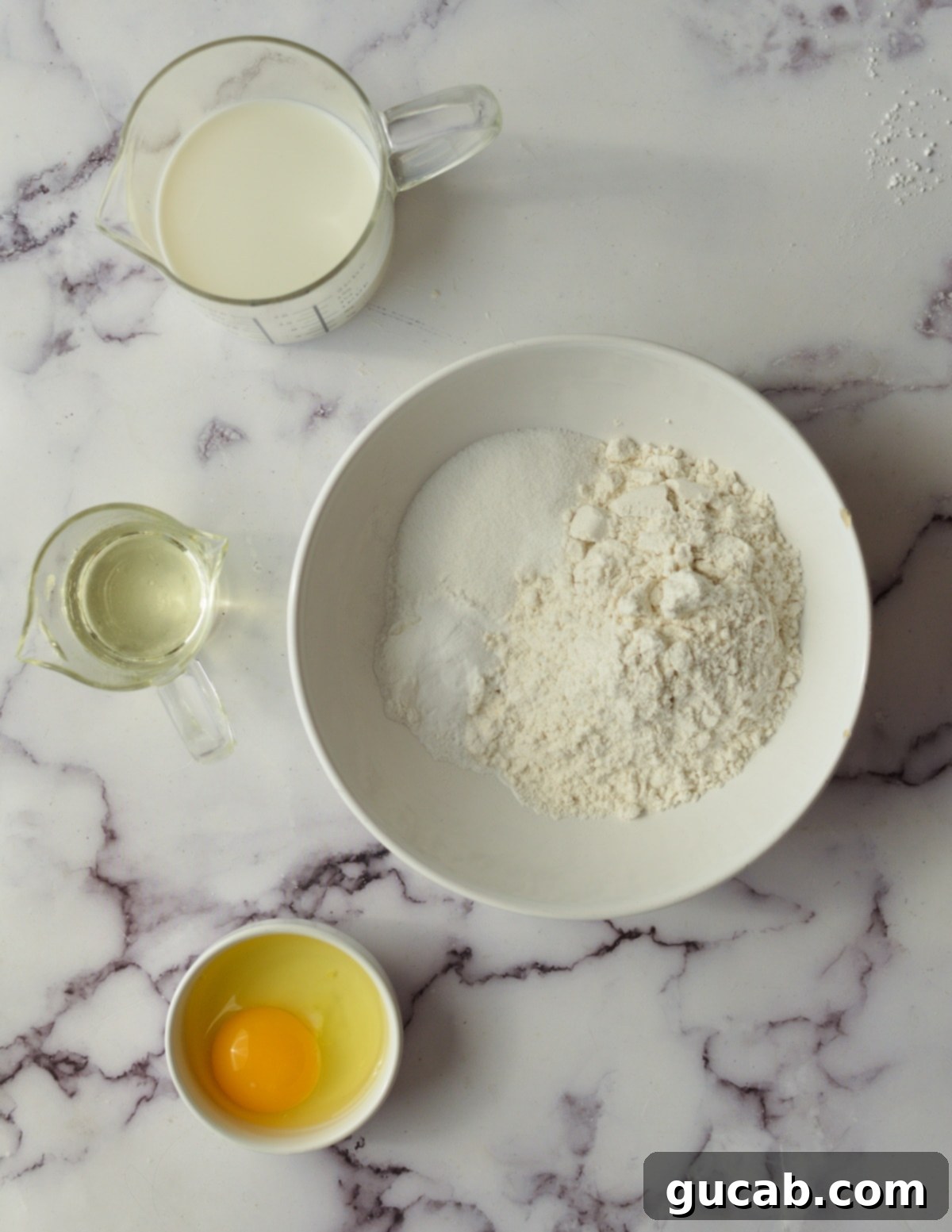 A collection of fresh ingredients for pancakes, including flour, milk, eggs, and oil, laid out on a surface.