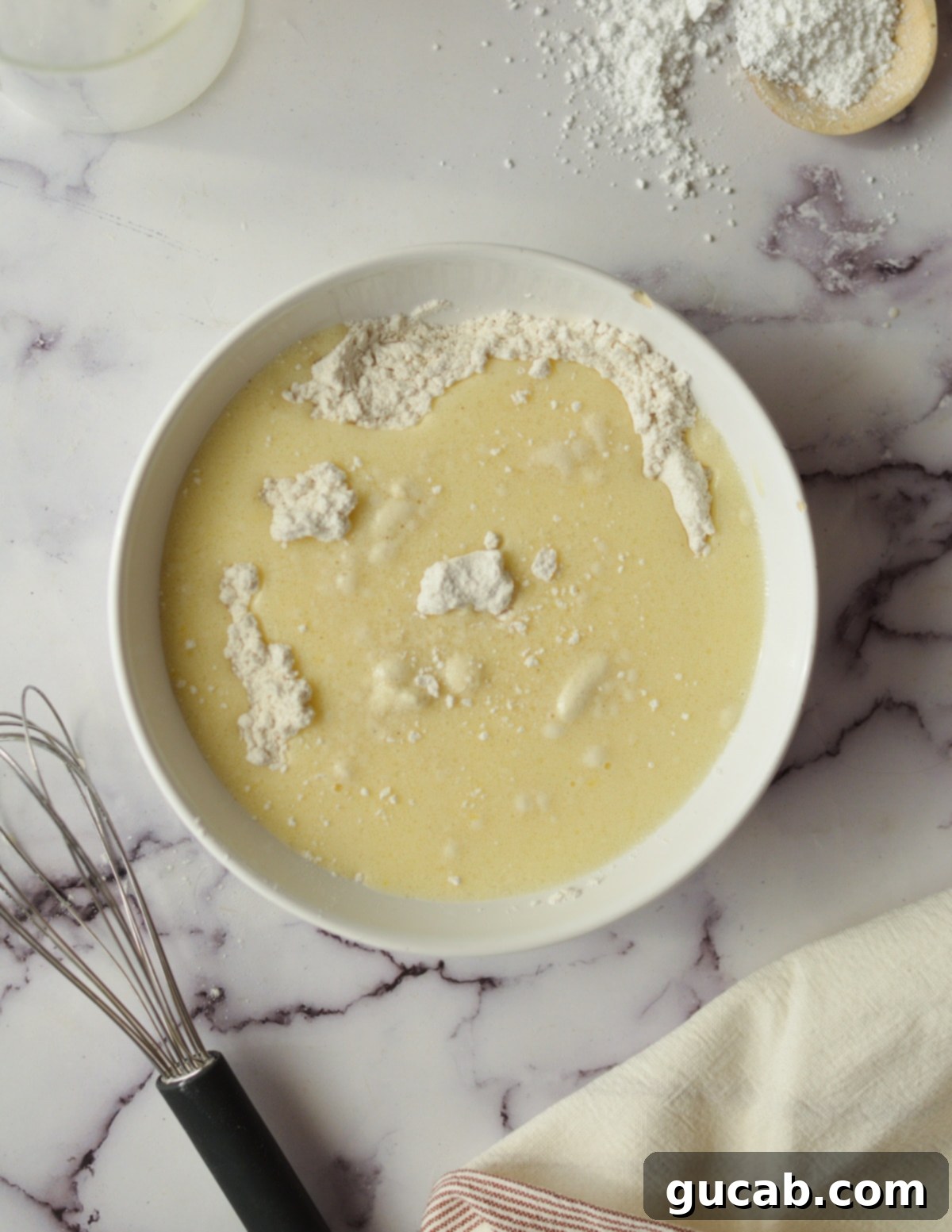 A bowl containing flour, with milk being poured in and an egg visible, indicating the start of mixing wet and dry ingredients.