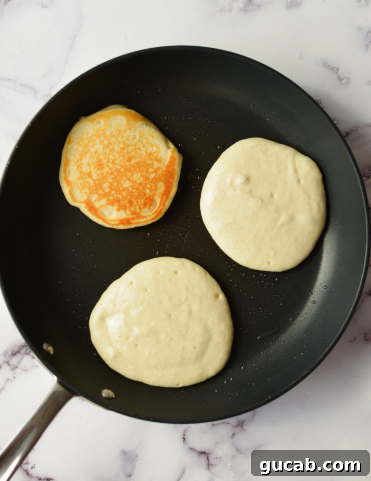 Several gluten-free pancakes cooking evenly in a hot skillet, with small bubbles forming on their surface.