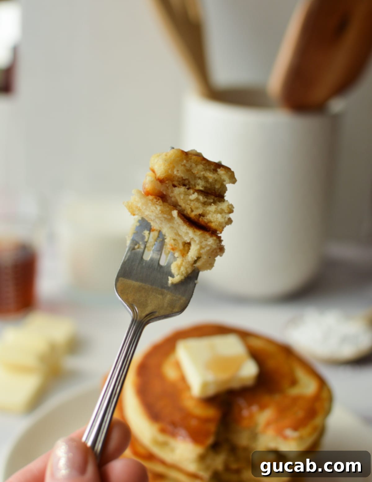 A close-up of a fork taking a bite out of a stack of fluffy gluten-free pancakes, revealing their airy interior.