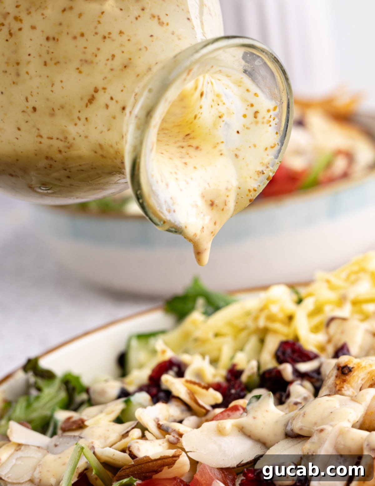 pouring honey mustard dressing onto a mixed greens salad 