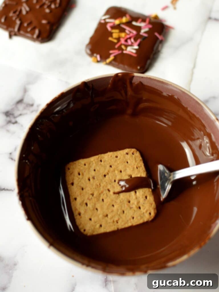 A graham cracker being submerged into a bowl of rich, melted chocolate, getting ready for its delicious transformation.