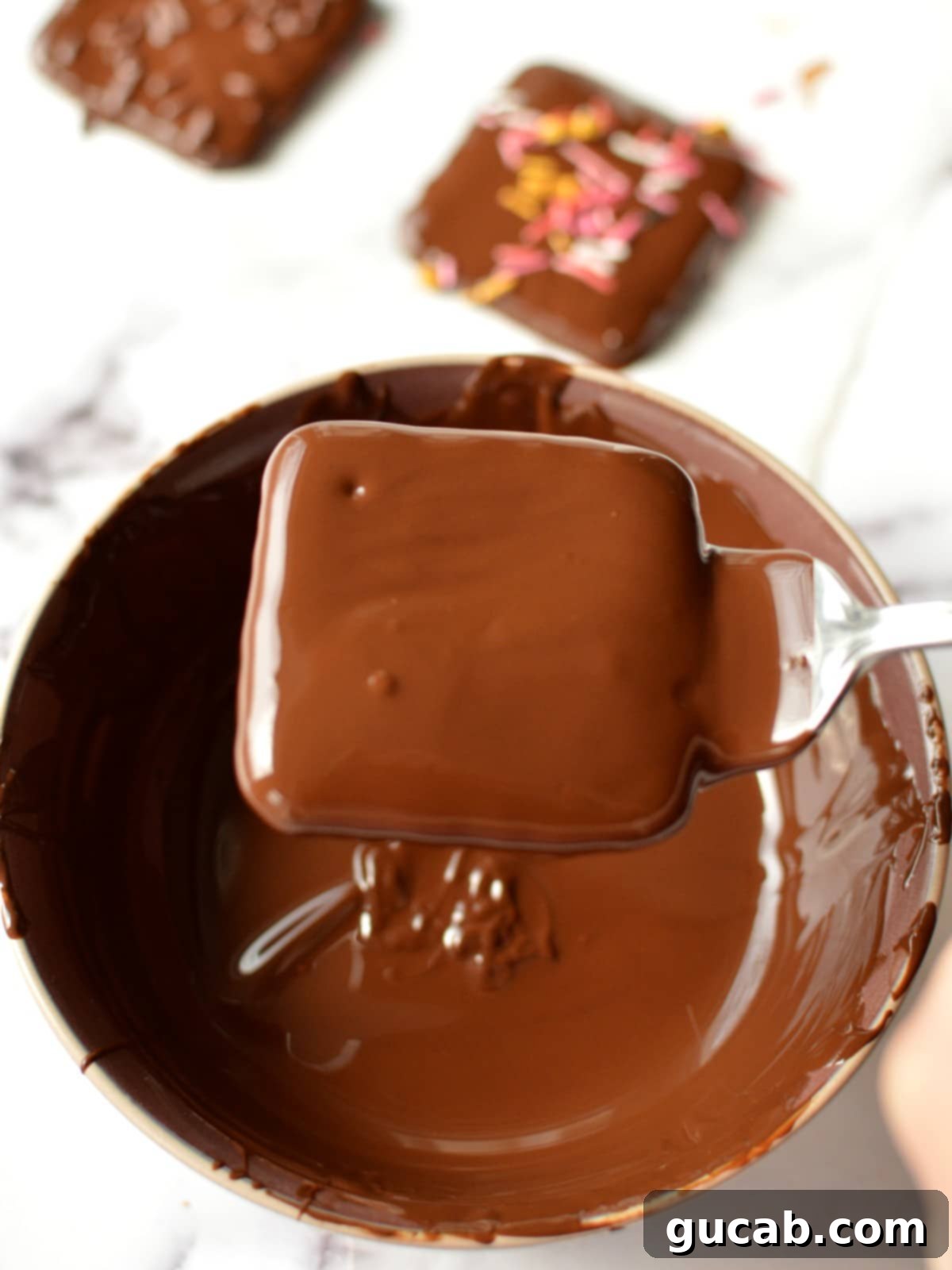 A chocolate covered graham cracker being carefully lifted from the melted chocolate, allowing excess to drip off for a clean finish.