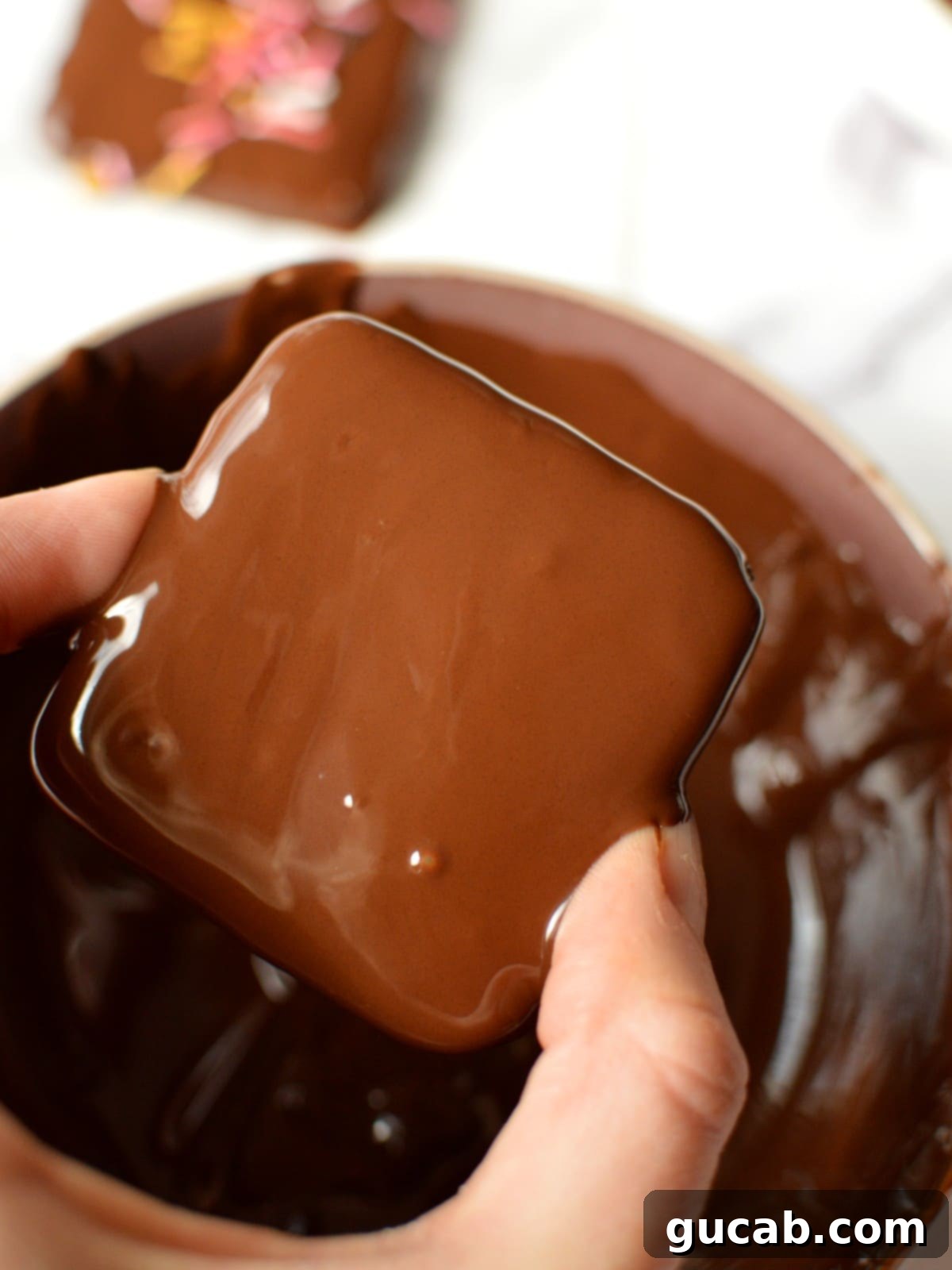 A hand gently placing a freshly chocolate covered graham cracker onto parchment paper, ready for toppings.