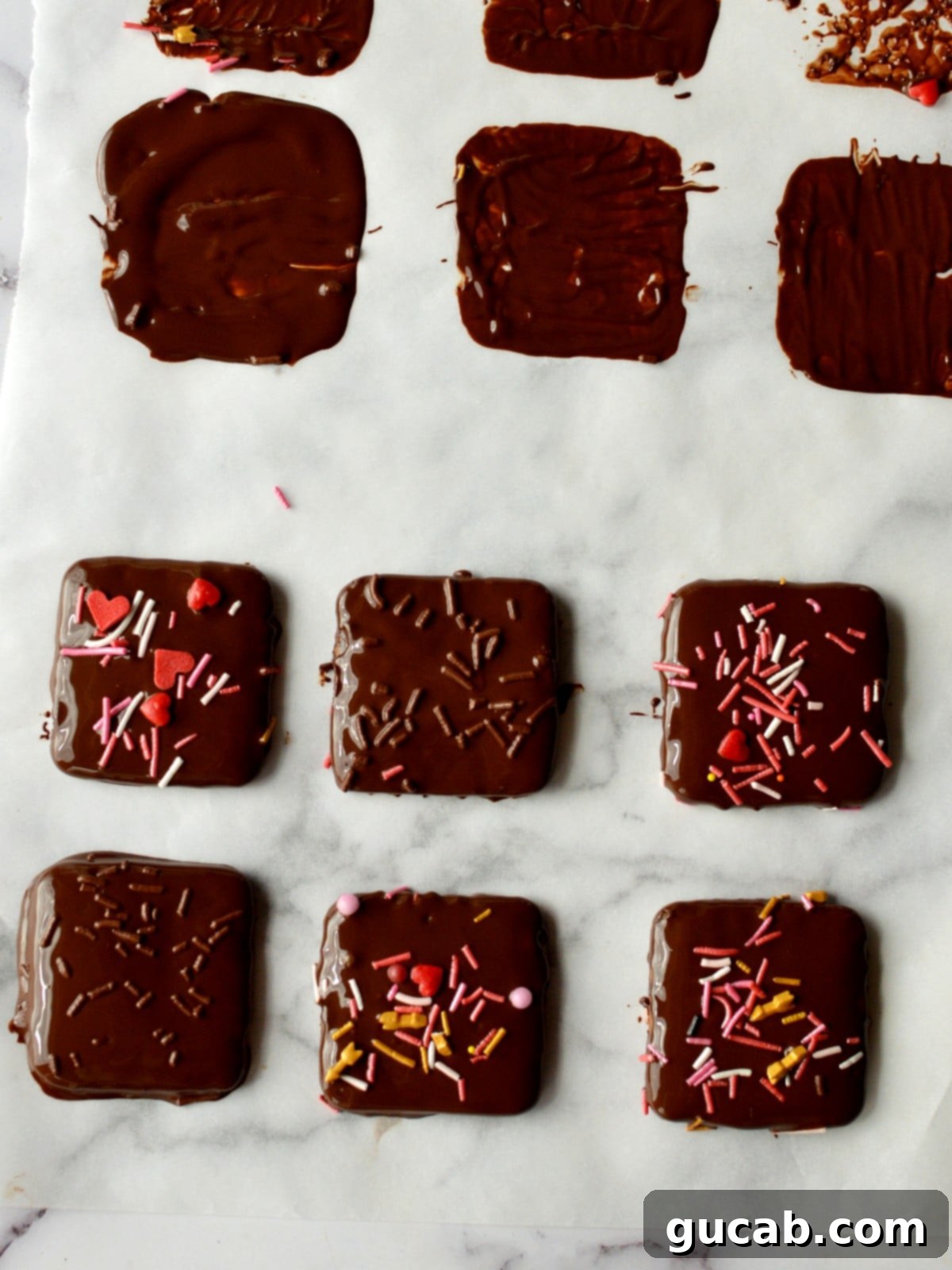 A selection of beautiful dark chocolate covered graham crackers with colorful sprinkles, laid out on parchment paper to set.
