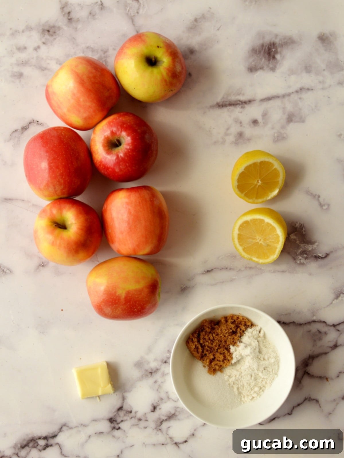 Fresh ingredients laid out: crisp pink lady apples, a bright lemon, rich butter, and a blend of brown and white sugar – all essential for a delightful apple pie.