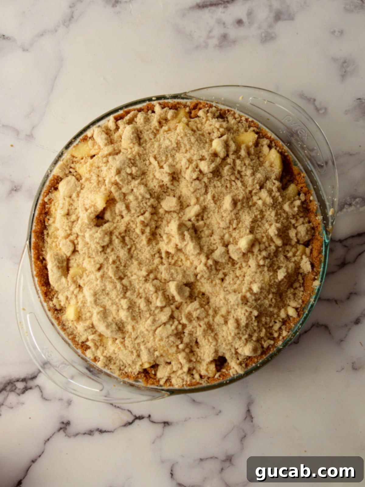 An unbaked apple pie in a graham cracker crust, generously filled with a pre-cooked apple mixture and ready for its crumb topping.