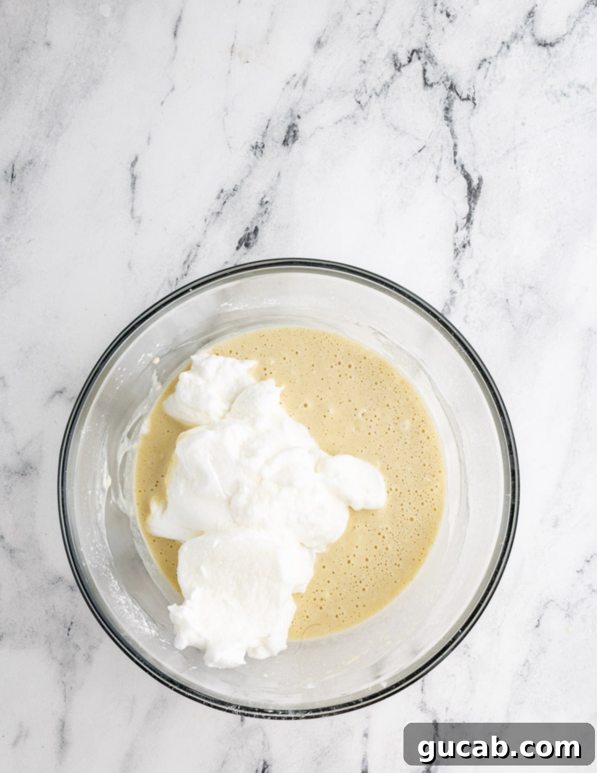 A bowl of gluten-free waffle batter with a layer of fluffy whipped egg whites resting on top, ready for folding.