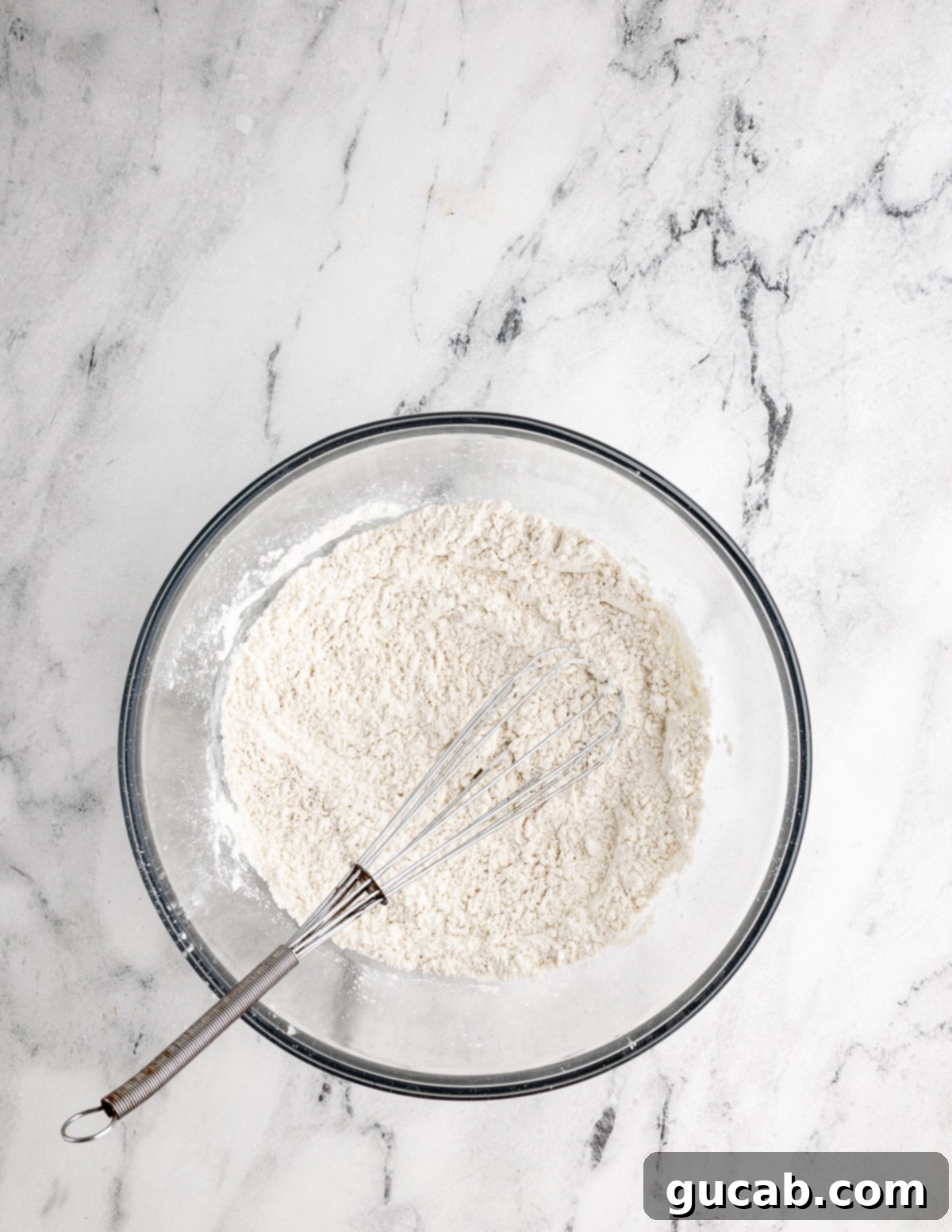A large bowl containing dry gluten-free waffle ingredients, with a whisk resting in the flour mixture, ready for the next step.