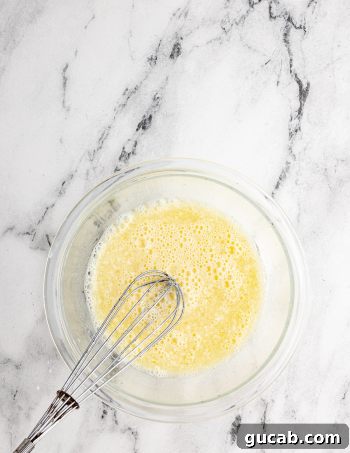 Your New Favorite Gluten-Free Waffle Recipe 6 A clear bowl holding a whisked mixture of eggs, oil, buttermilk, and milk, forming the wet ingredients for the waffle batter.