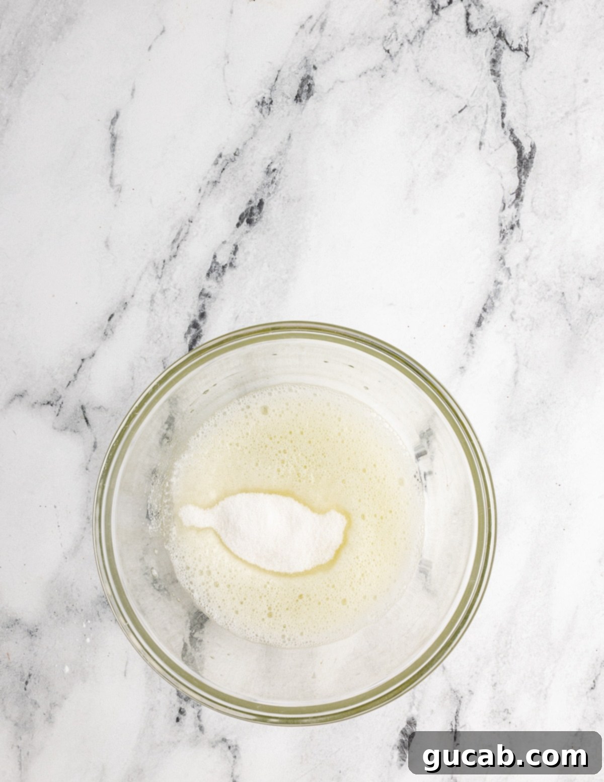 A bowl of frothy egg whites with granulated sugar sprinkled over the top, ready to be whipped further.