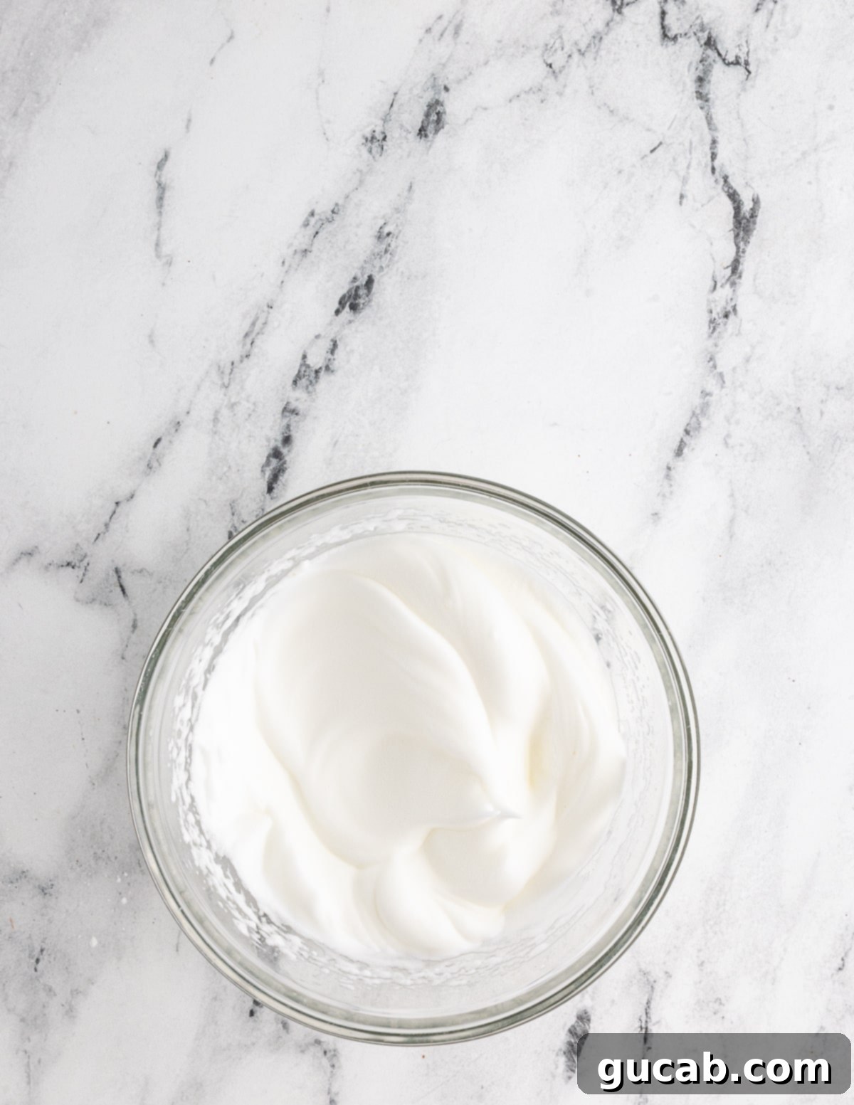 A bowl of perfectly whipped egg whites showing stiff, glossy peaks, indicating they are ready for folding into the batter.