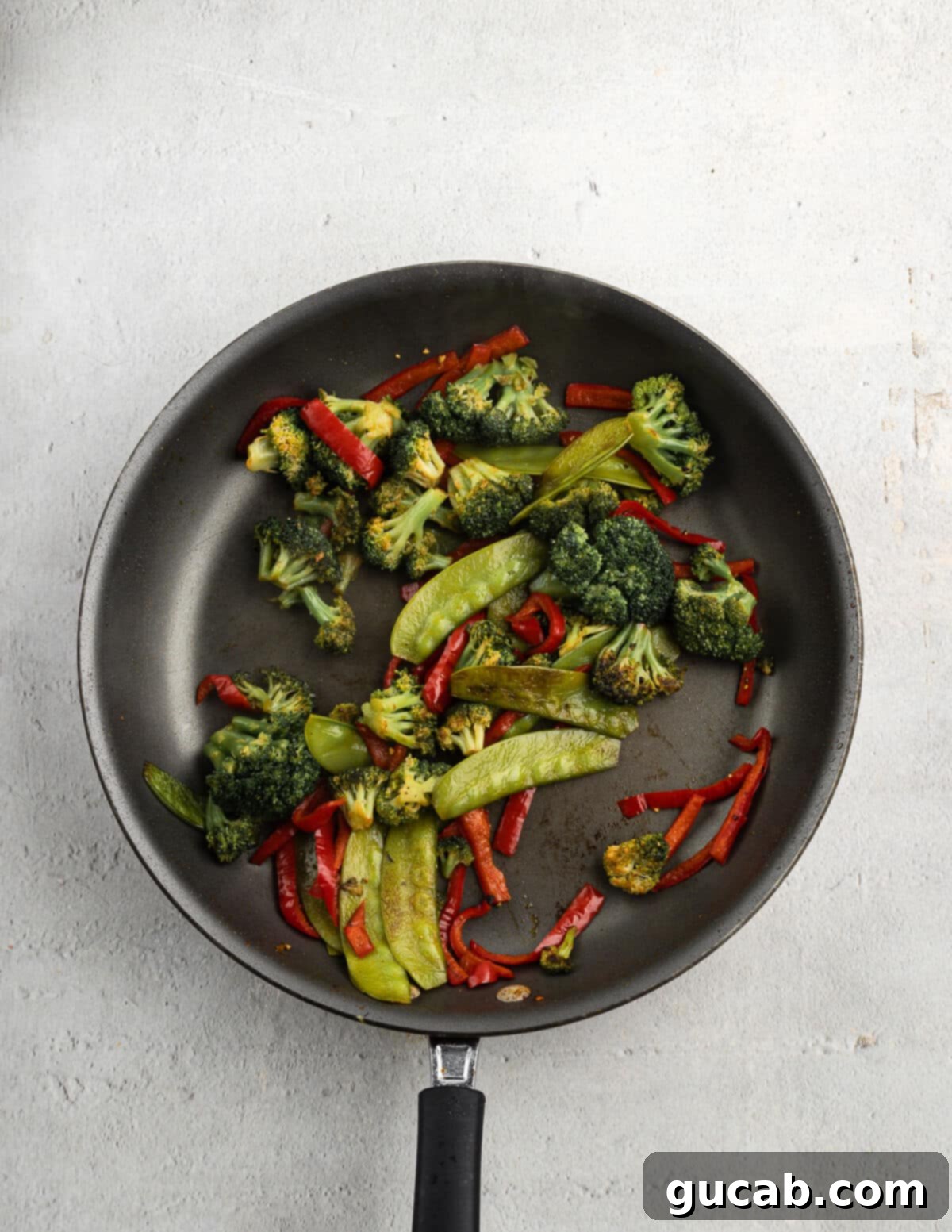 Sautéed broccoli, bell peppers, and snap peas in a skillet, slightly softened but still retaining a pleasant crispness, indicating they are nearly ready for the next ingredients.