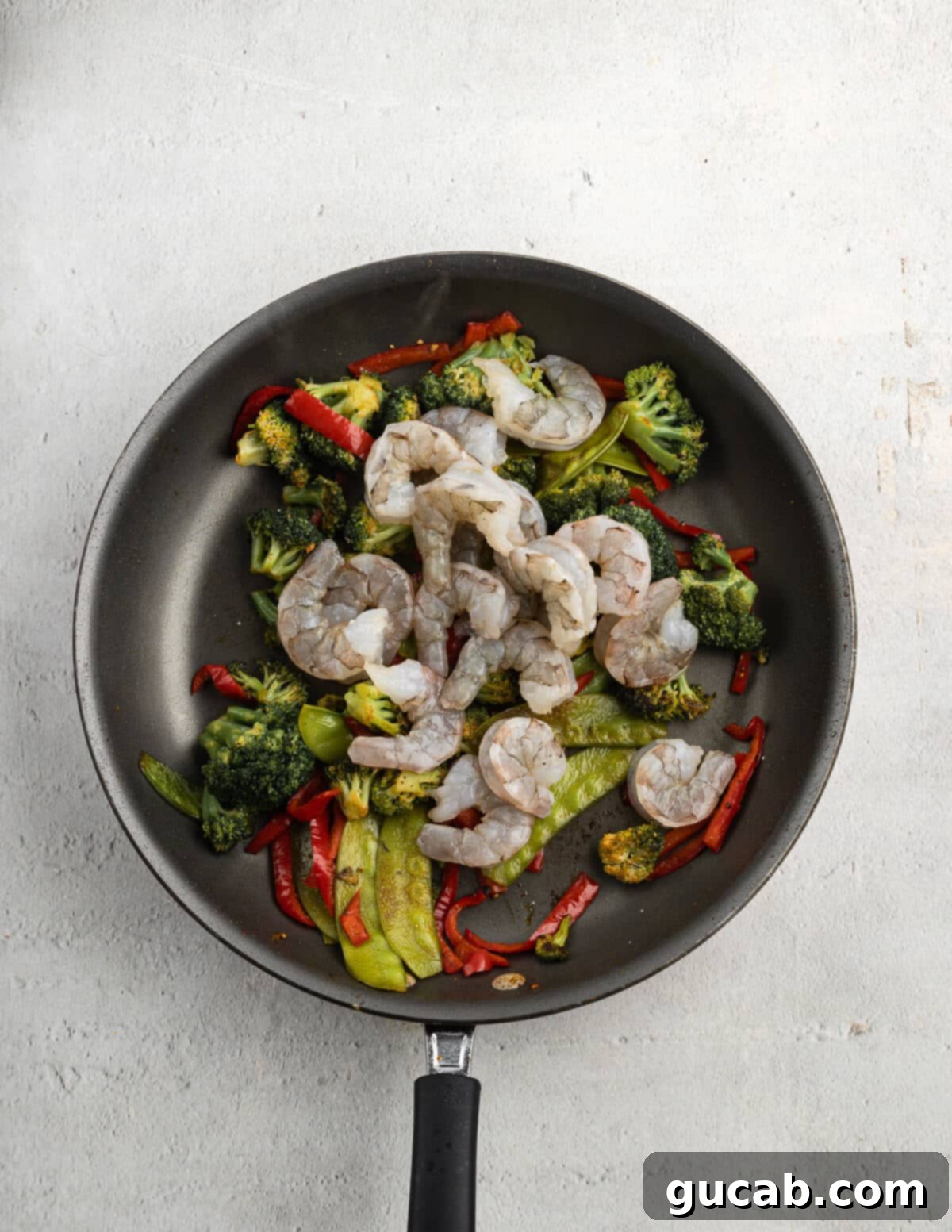 Vibrant sautéed vegetables in a skillet with raw shrimp just added on top, ready for quick cooking to achieve perfect tenderness.