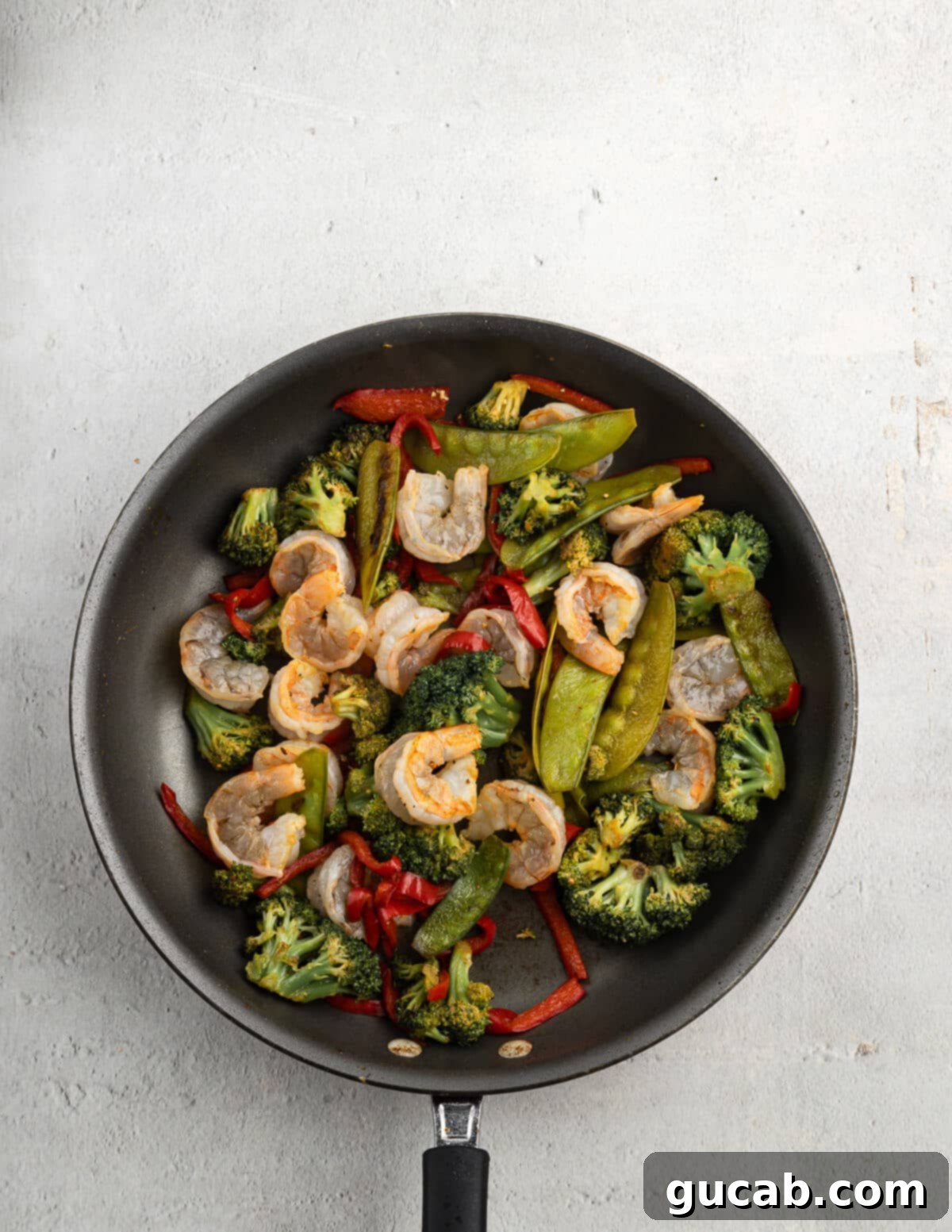 Sautéed vegetables and partially cooked shrimp in a skillet, showing the shrimp turning pink as they cook, signaling readiness for the final stages of the stir fry.