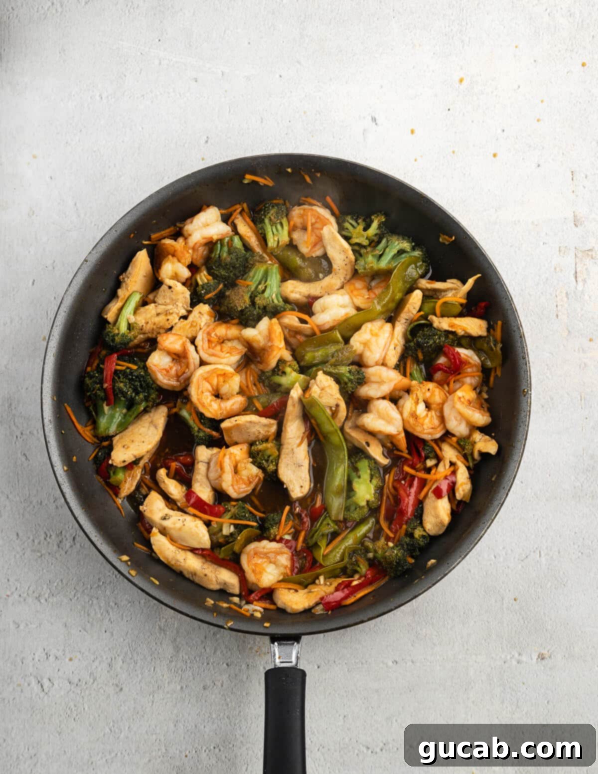 A large skillet brimming with the complete chicken and shrimp stir fry, featuring all the vibrant vegetables and proteins coated in the glossy, thickened sauce.