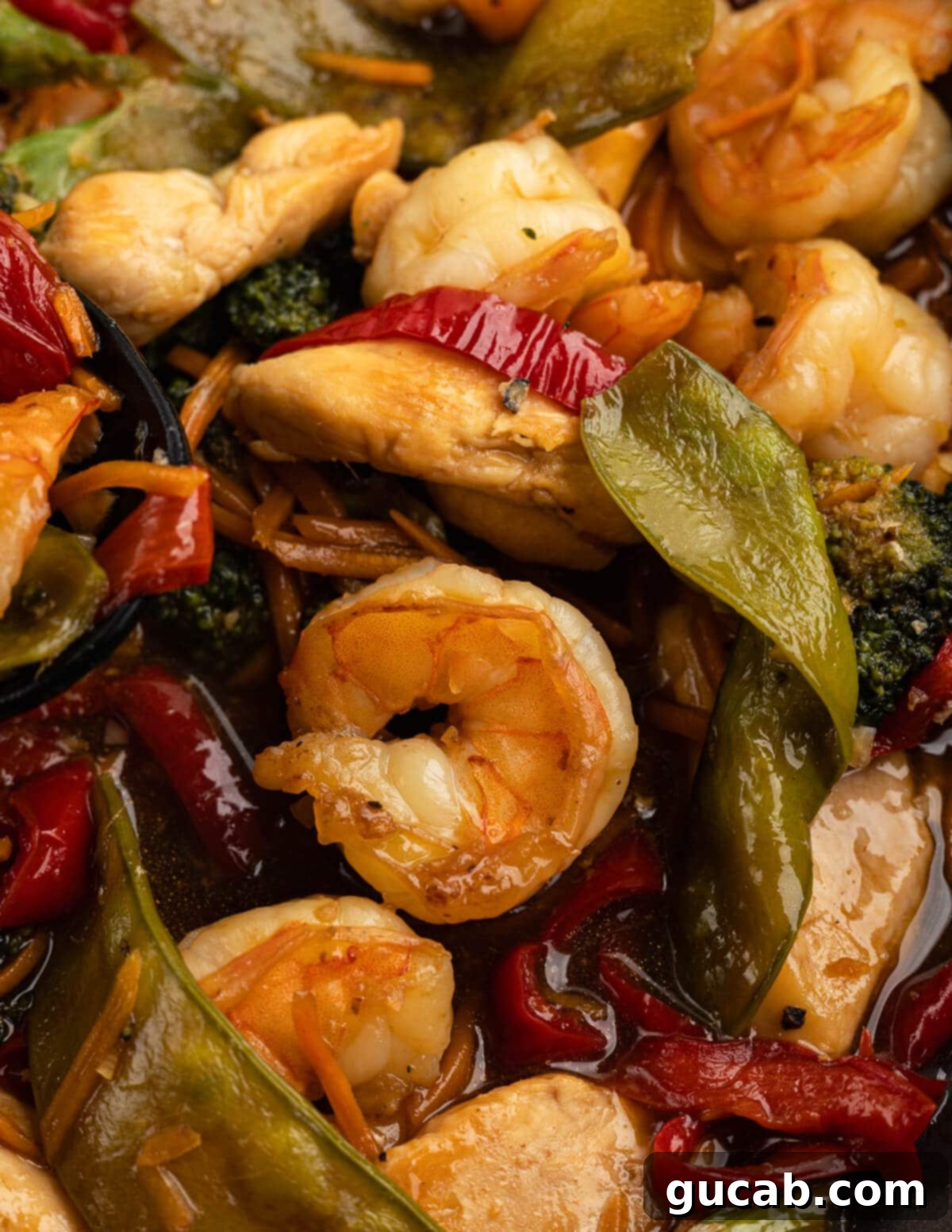 Close-up shot of a sizzling chicken and shrimp stir fry in a skillet, highlighting colorful bell peppers, crisp broccoli, and tender snap peas glistening in the rich sauce.