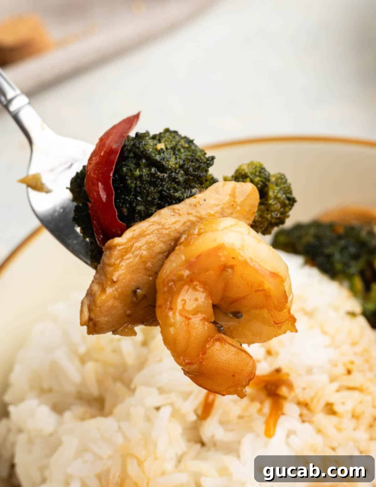 A forkful of perfectly cooked chicken and shrimp stir fry, showcasing tender broccoli, juicy chicken, succulent shrimp, and bright bell pepper, ready to be enjoyed.