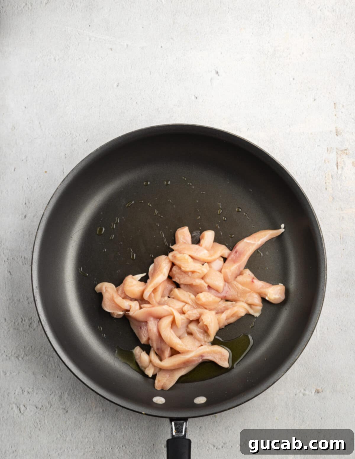 Thinly sliced chicken strips beginning to sizzle and cook in a hot nonstick skillet, seasoned and preparing to brown.