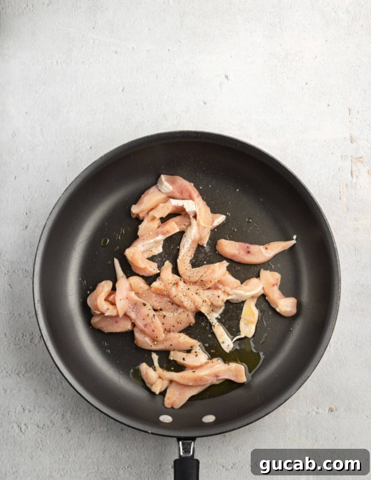 Partially cooked, lightly browned sliced chicken pieces in a hot skillet, showing the initial stages of searing for a tender result.