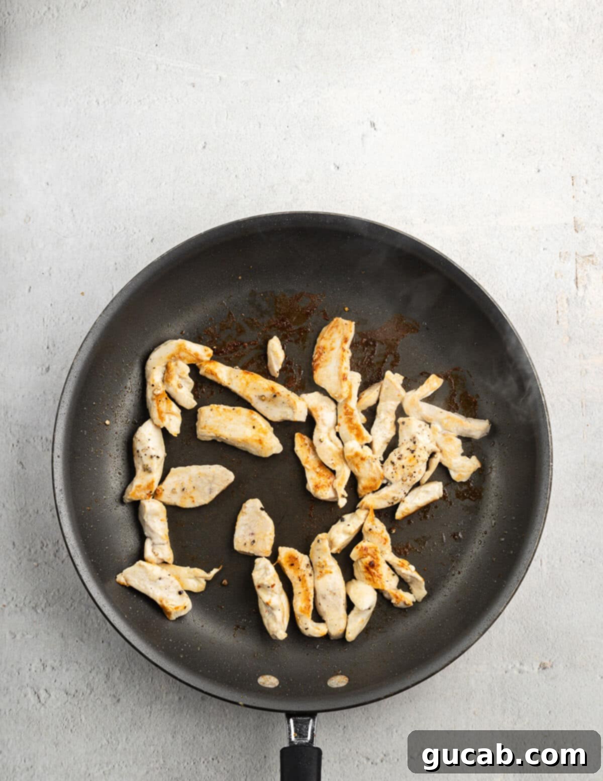 Small, perfectly cooked chicken pieces in a skillet, ready to be removed to prevent overcooking before the vegetables are added.