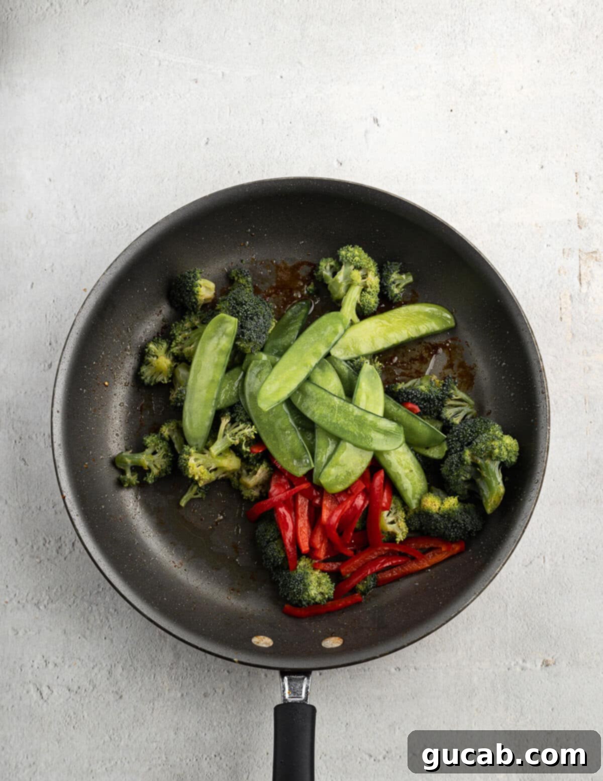 Fresh broccoli florets, crisp snap peas, and vibrant bell pepper strips introduced into a hot skillet with olive oil, ready to begin sautéing.