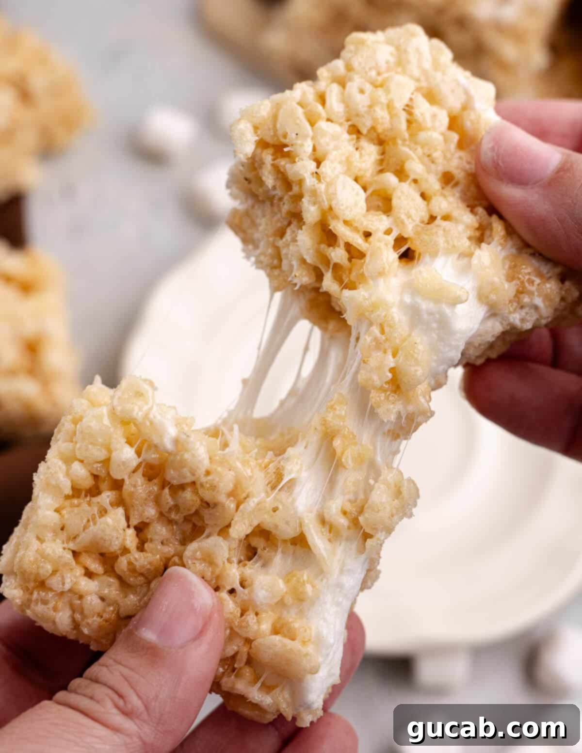 Hand pulling apart a perfectly gooey homemade rice crispy treat, revealing its stretchy marshmallow texture.