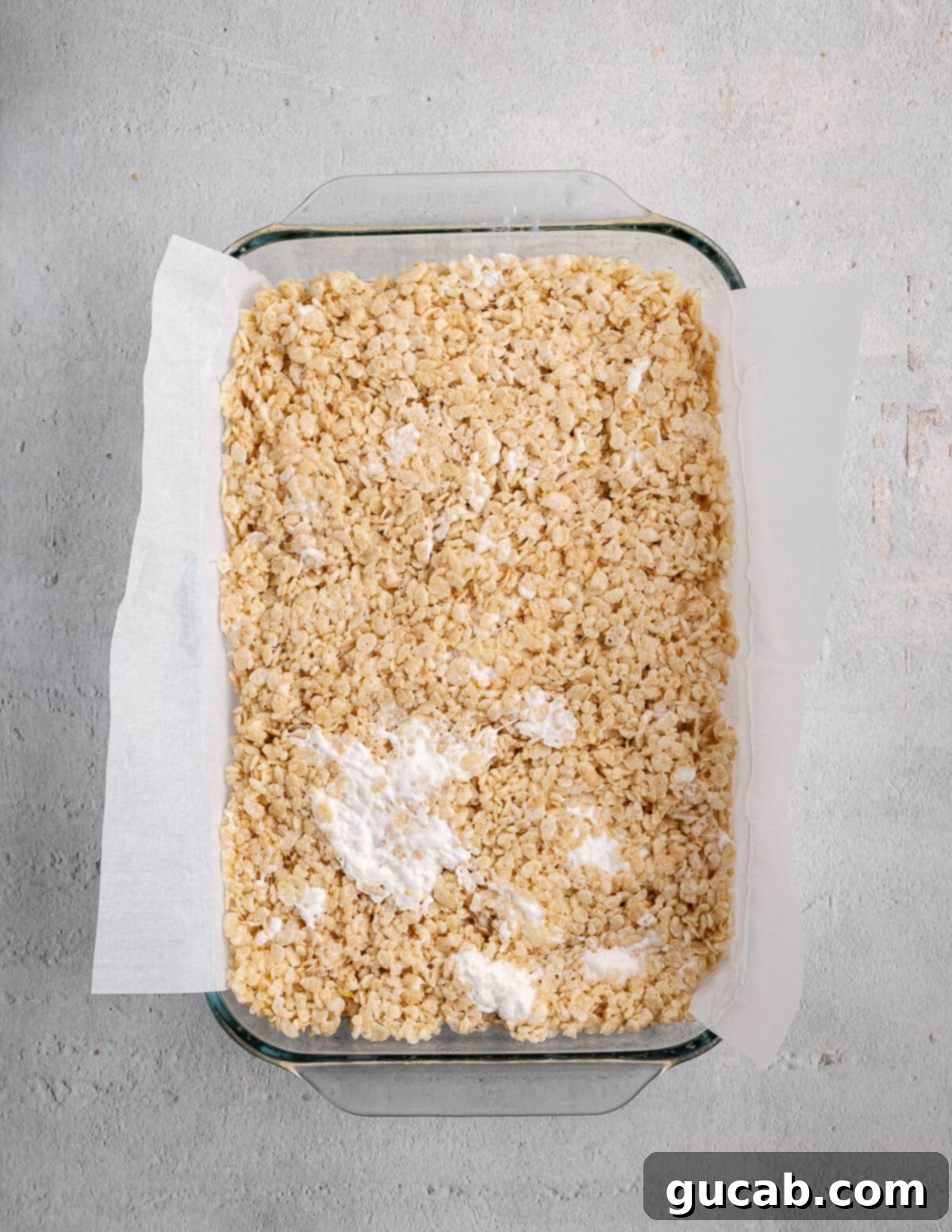 Uncut homemade rice krispie bars perfectly spread and flattened in a baking dish, ready to set.