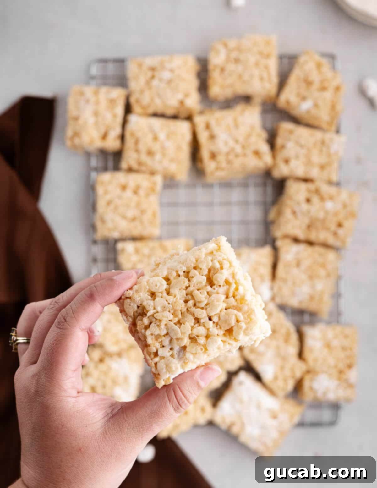 A hand holding a single homemade rice krispie bar, showing its inviting texture.