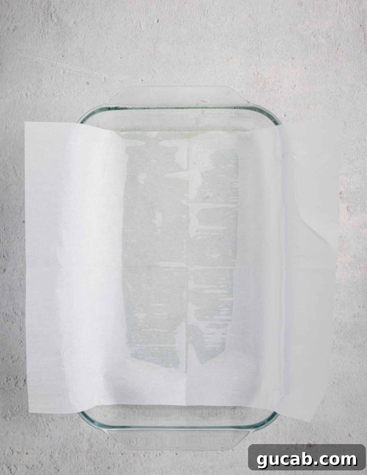 A glass baking dish lined with parchment paper, with the ends hanging over the sides for easy removal.